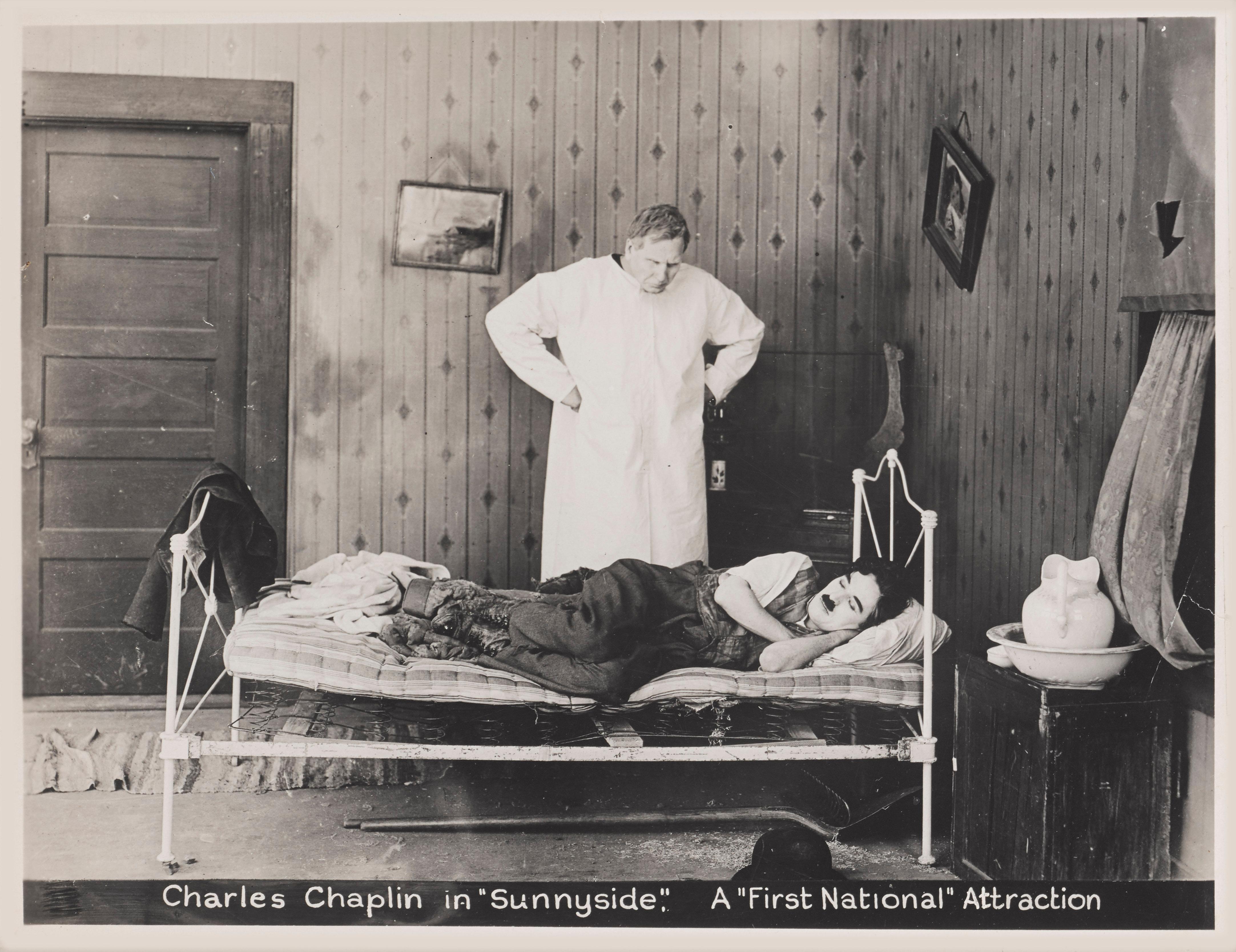 Original US production still for Charlie Chaplin and Edna Purviance 1919 silent comedy.
This early American short silent film was written by, directed by and stars Charlie Chaplin. In it Charlie works crazy hours at a hotel in rural Sunnyside, where