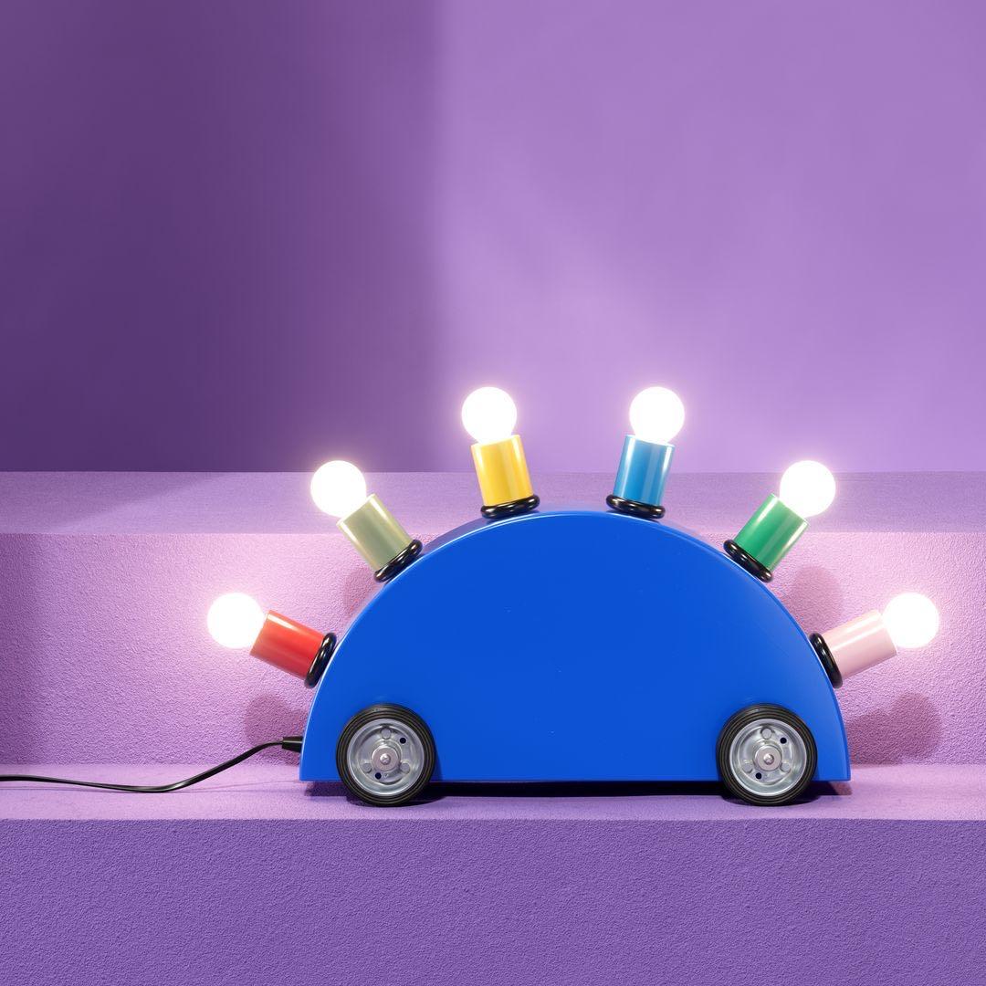 The Super lamp by the designer Martine Bedin can be dragged along like a dog on a leash (with an arched back resembling a stegosaurus), embodying the playful spirit of Memphis. It is made with a semicircle in lacquered fiberglass resting on four
