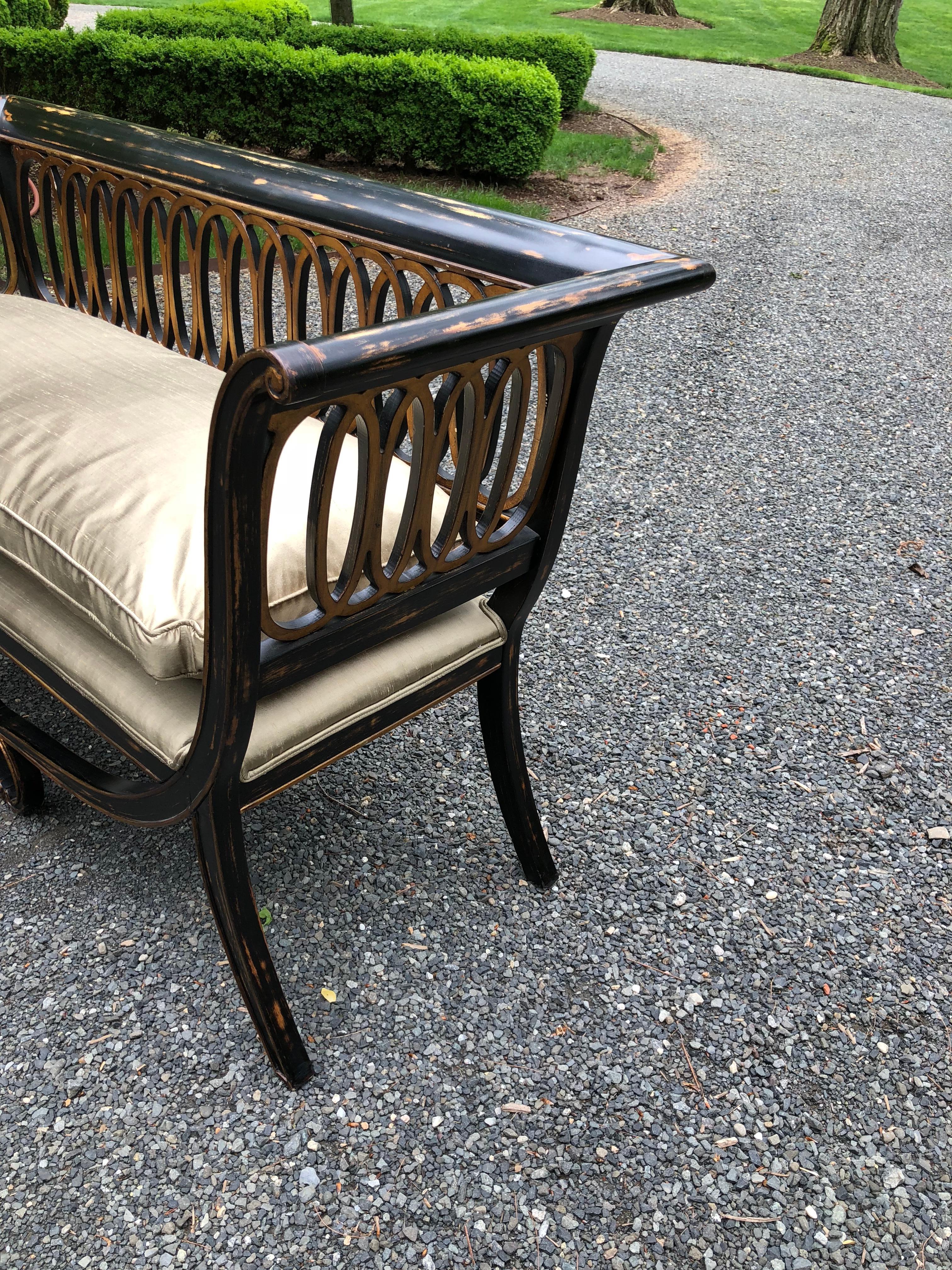 Very pretty and unusual Hollywood Regency settee. The wood has a beautiful patina in ebonized wood with hints of brown. The circular decoration is in a gilt finish as is the trim. The piece has recently been upholstered with a plush cushion in a