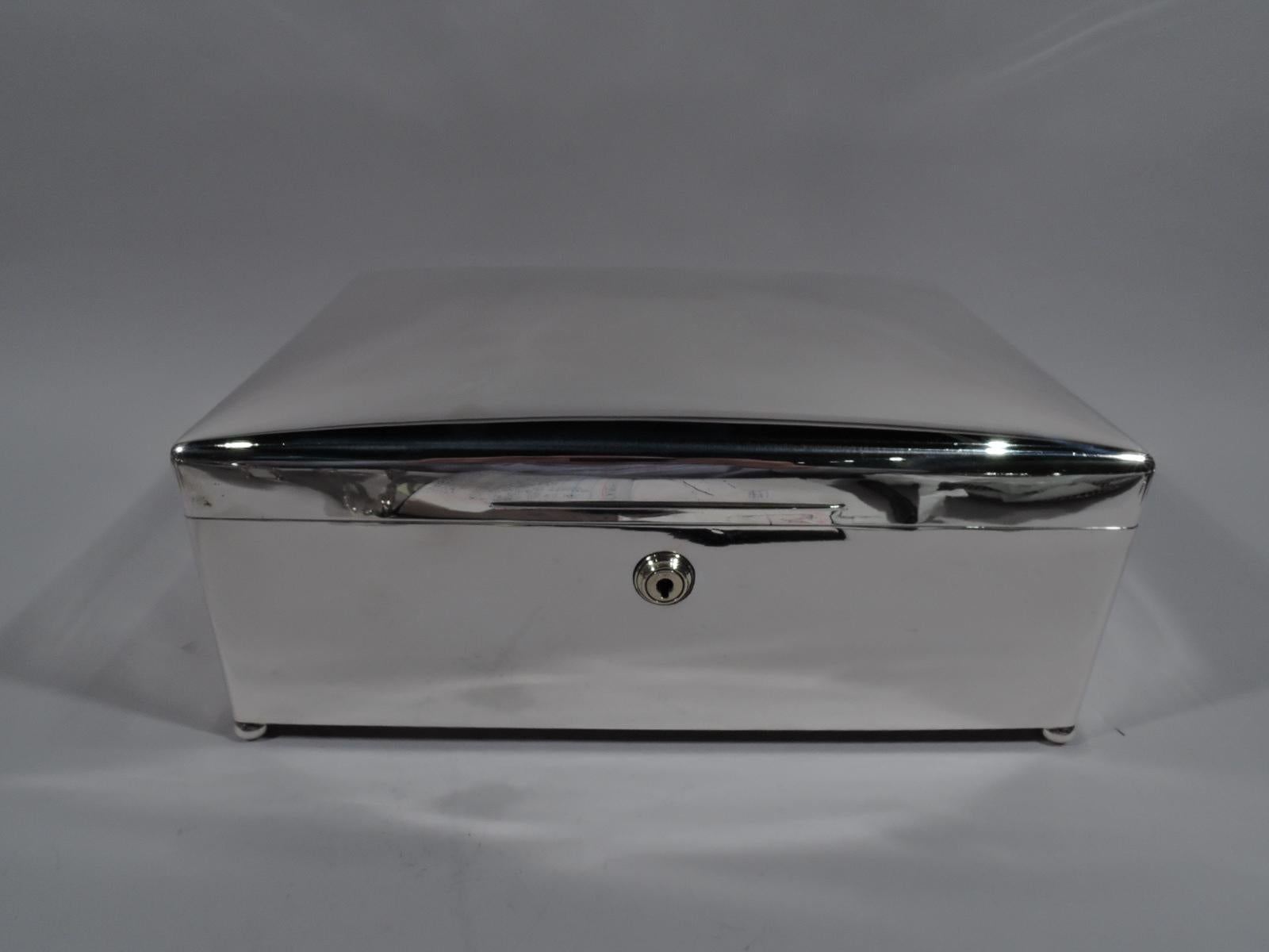 George V sterling silver cigar box. Made by Walker & Hall in London in 1912. Rectangular with straight sides and curved corners. Cover hinged and curved with tapering tab. Lock and key. Corner ball supports. Box interior cedar lined and partitioned.