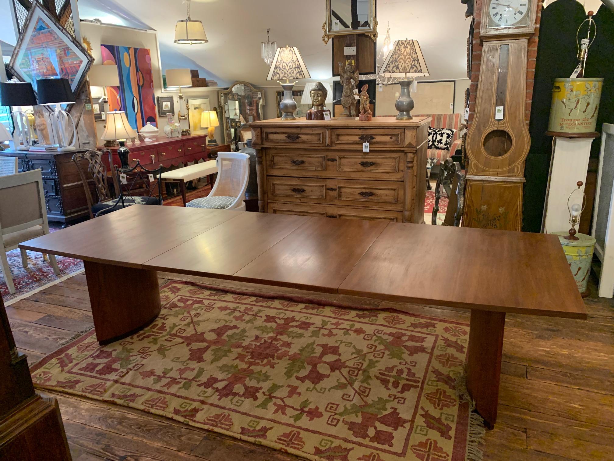 Stunning Mid-Century Modern very large sleek walnut dining table with 2 leaves that will extend the table to seat 12. Top with apron sits upon 2 half moon pedestals with a small ebonized trim at the base of each. Absolute simplicity at its most
