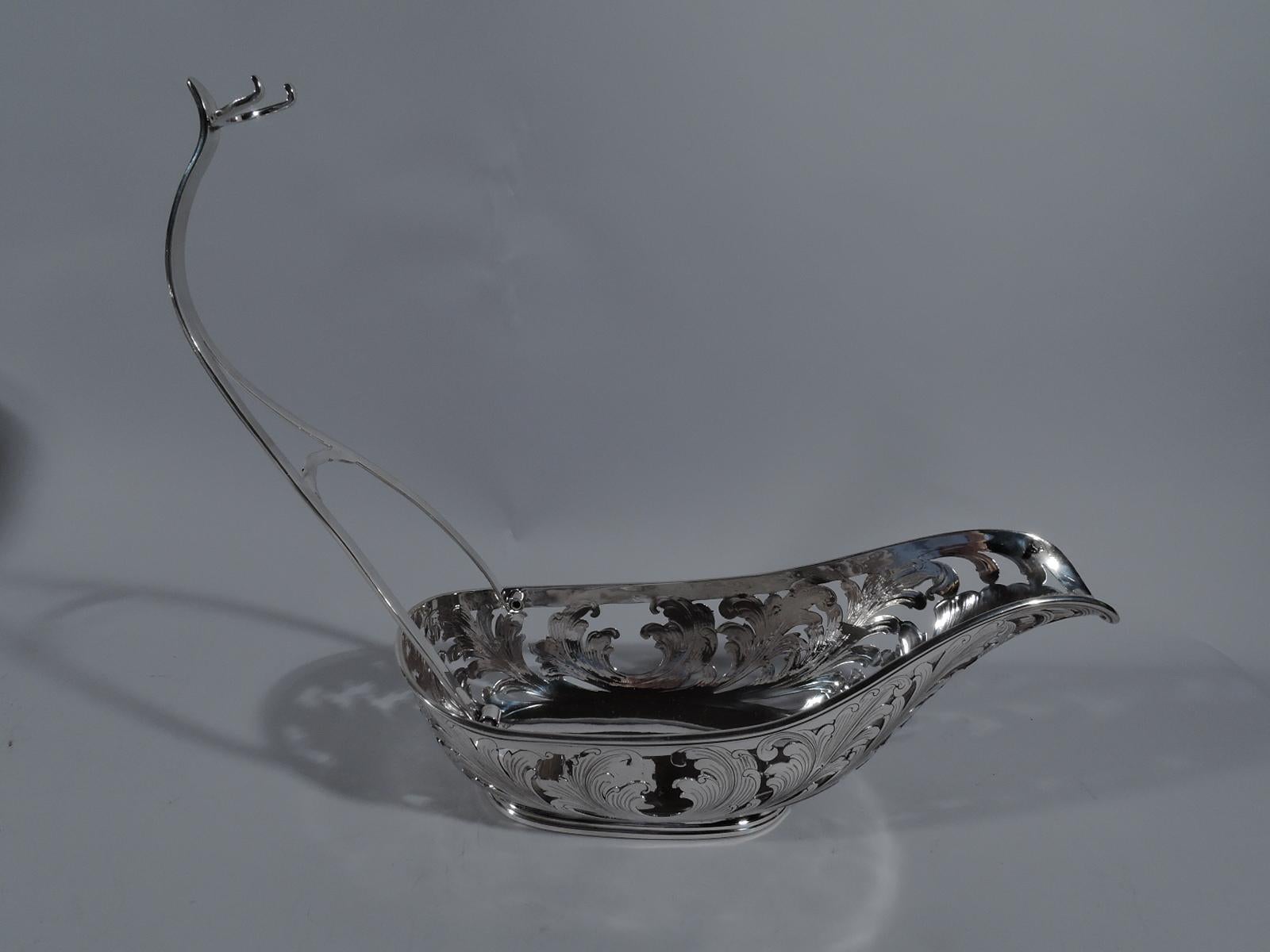Stylish sterling silver wine cradle. Made by Buccellati in Italy. Ovoid body with solid well. Sides open with fluid, scrolling engraved leaves. Handle hinged and open with C-scroll ring for securing bottle neck. Stepped oval foot. Marked “Buccellati