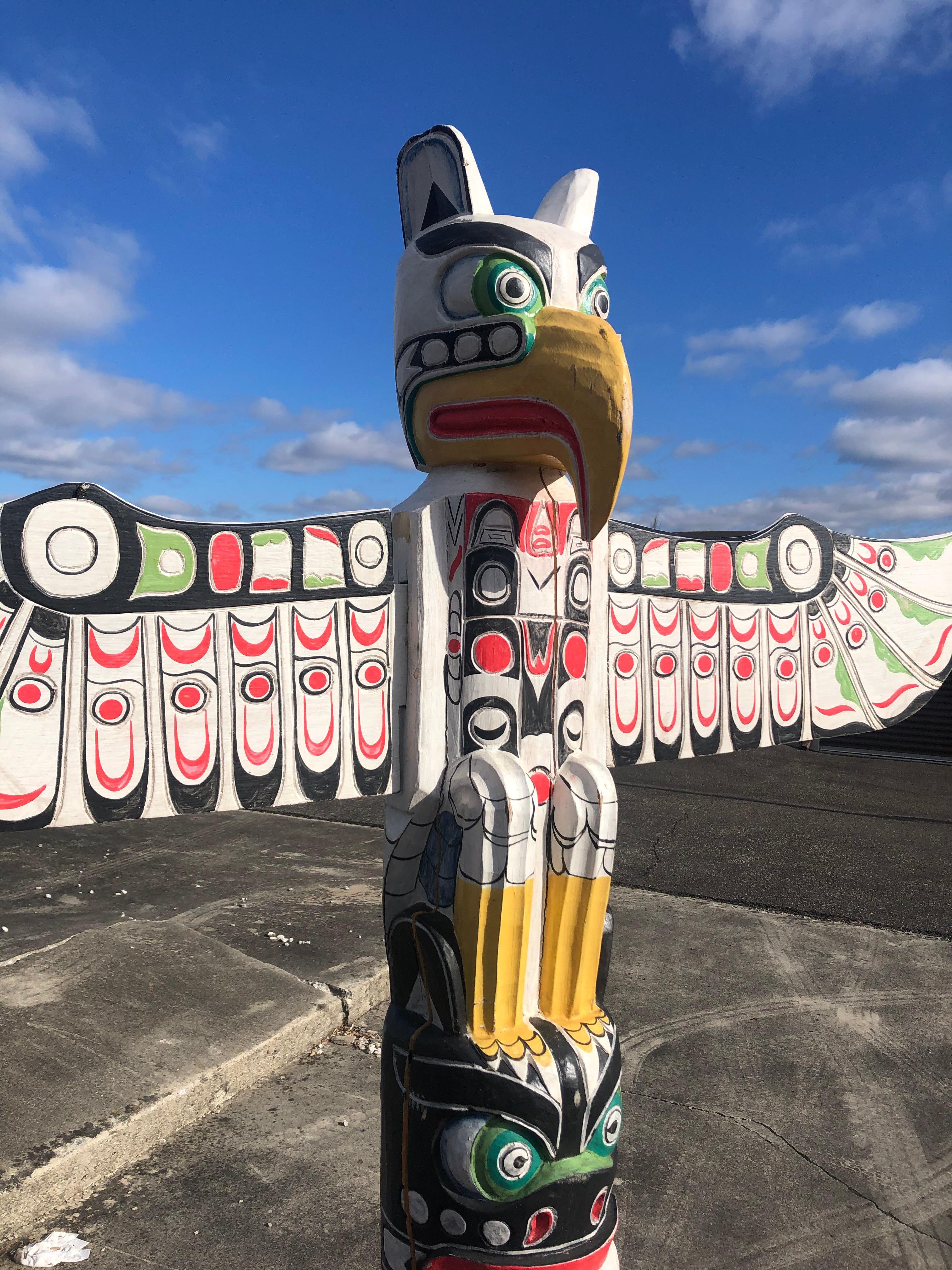 An eye-catching hand carved tribal TOTEM pole having bold color palette in black, red, green and white and yellow, fabulous bird like head with prominent hooked beak, and an impressive span of outstretched wings.