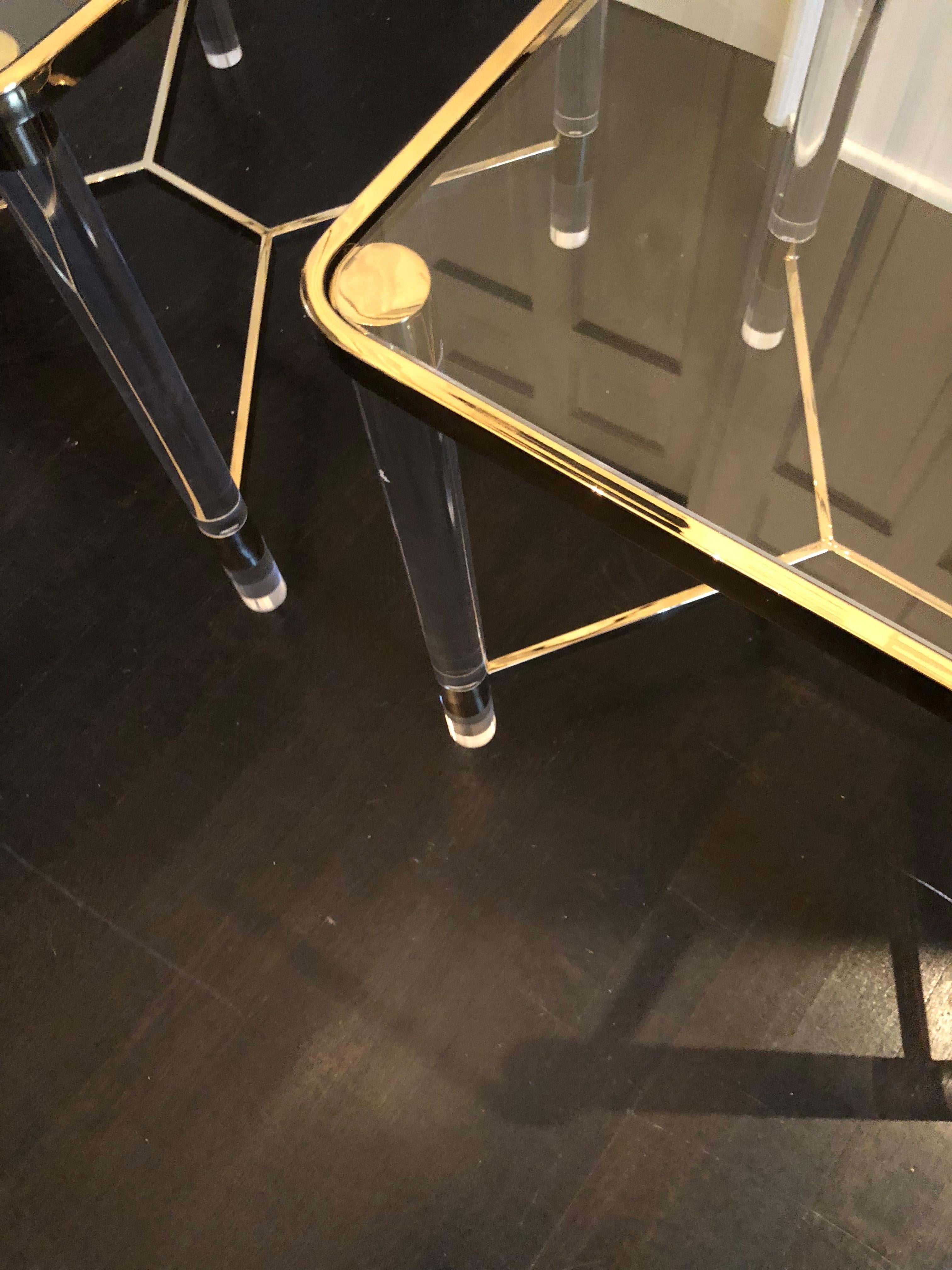 Stunning pair of Lucite and brass end tables with glass tops. Each table has thick Lucite legs capped in brass with a brass stretcher at the base. Tables are versatile and would work in several decors. Unsigned.