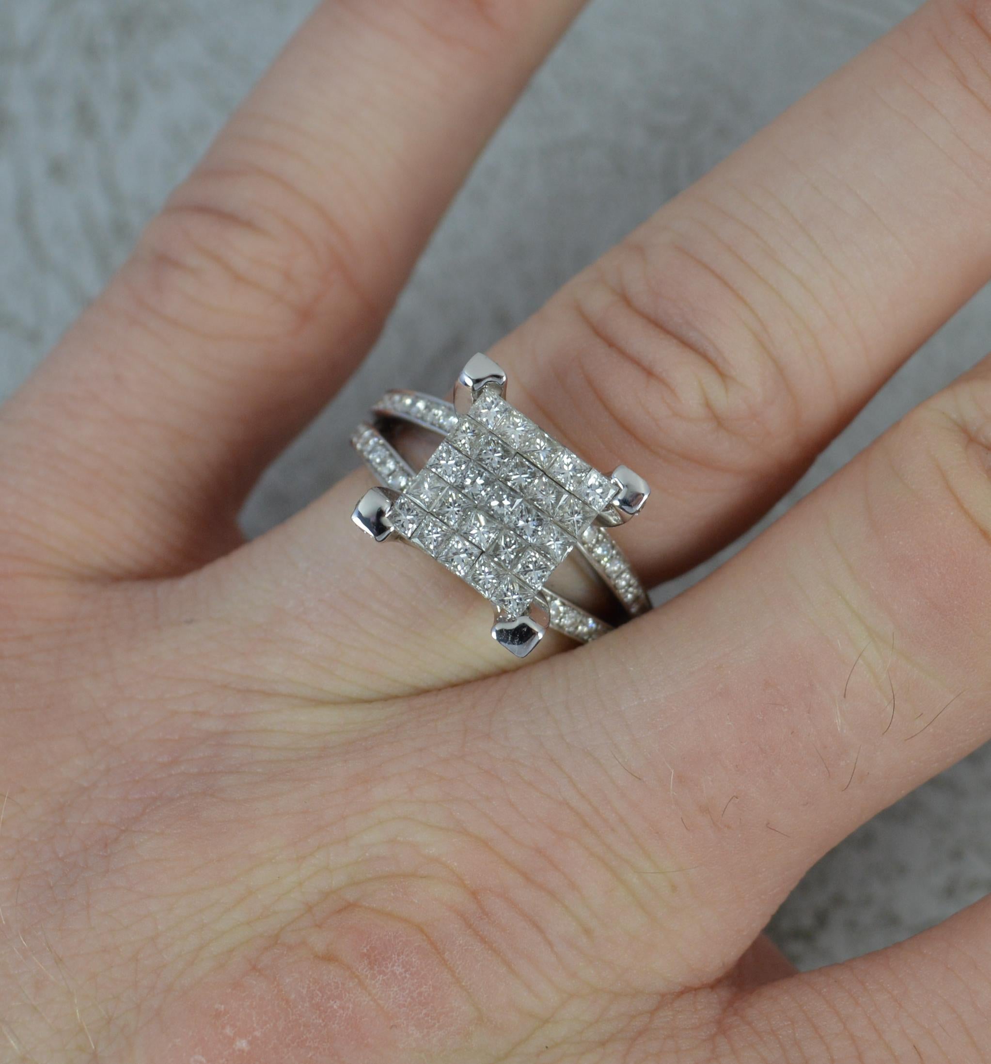 A highly impressive diamond cluster ring.
Solid 18 carat white gold example.
Designed with a 5x5 grid of princess cut diamonds to the centre. 9.5mm x 9.5mm with four corner sections.
A split, two row, diamond pave set shoulders with many additional