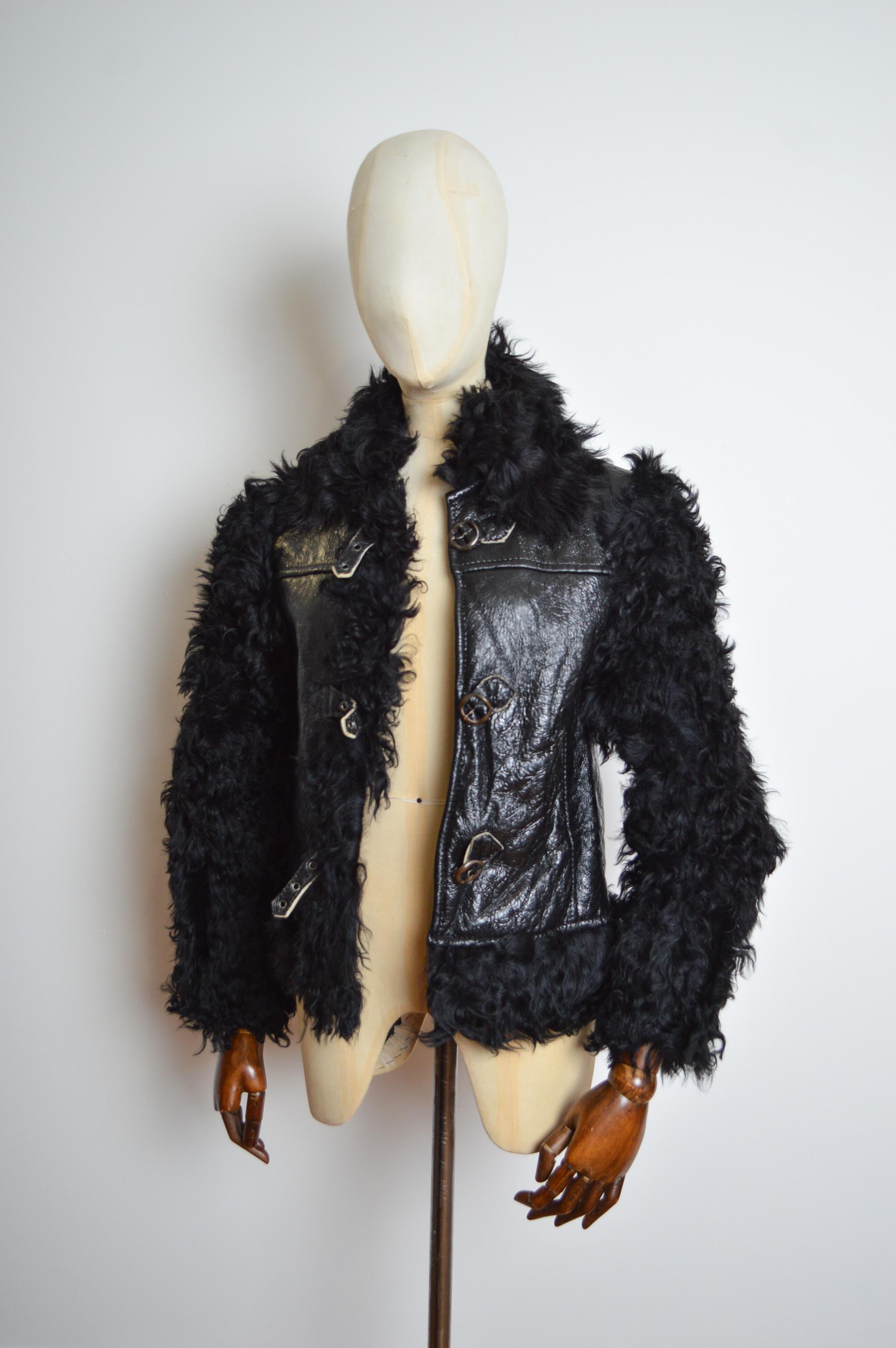An excellent example, this 1960s Vinyl Shearling coat features a shiny patent black body intercepted with Thick curly sheepskin trimmed panels and full shearling sleeves, Buckles down the front and soft cream sheepskin lined interior body. 
Pit to