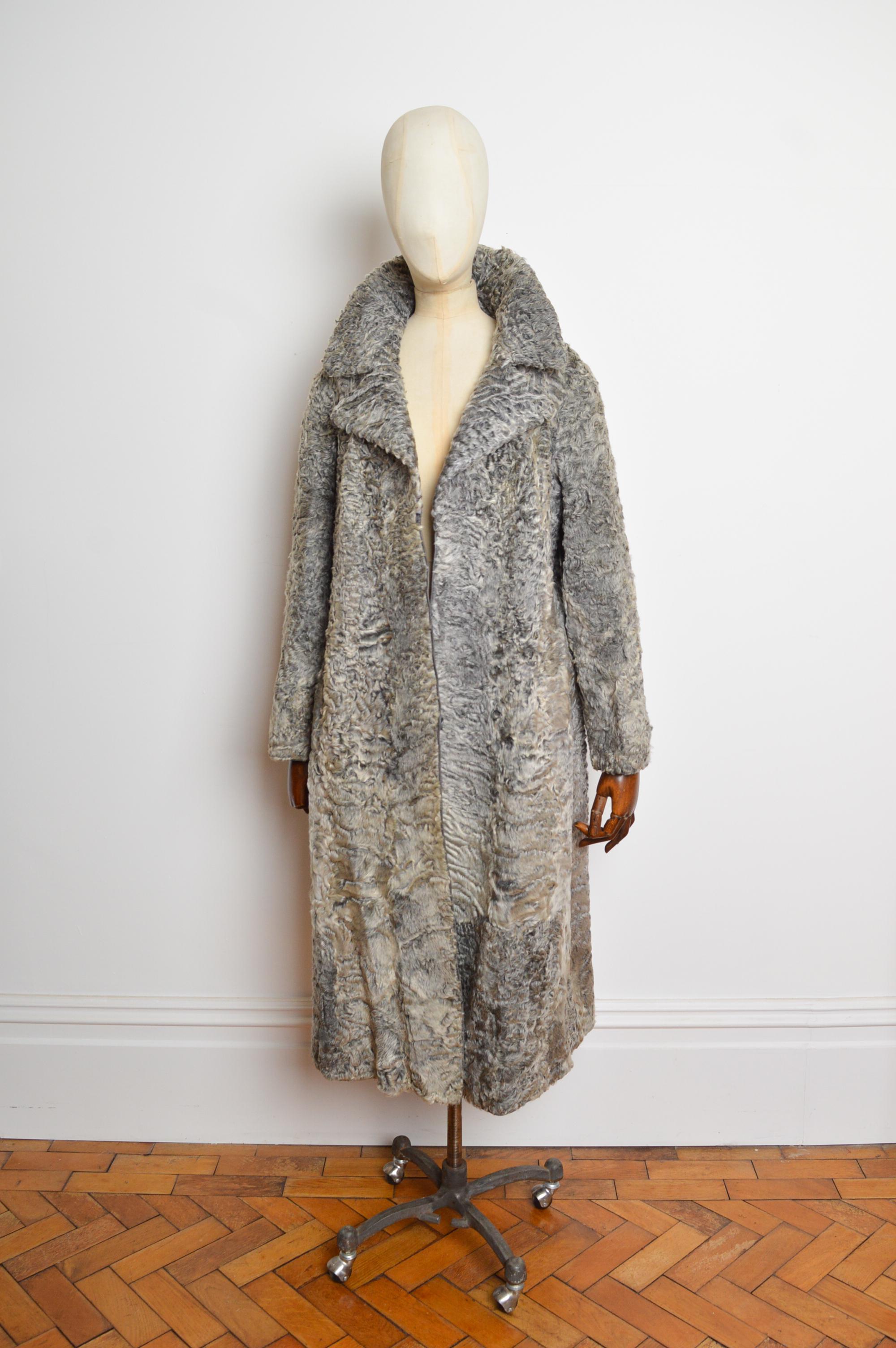 Un decadente cappotto Astrakhan degli anni '70. Realizzato con enormi pellicce di astrakan morbide come la seta, con finiture interne in pelle di agnello, fodera in rayon satinato grigio e chiusura con gancio al centro. I revers della giacca possono