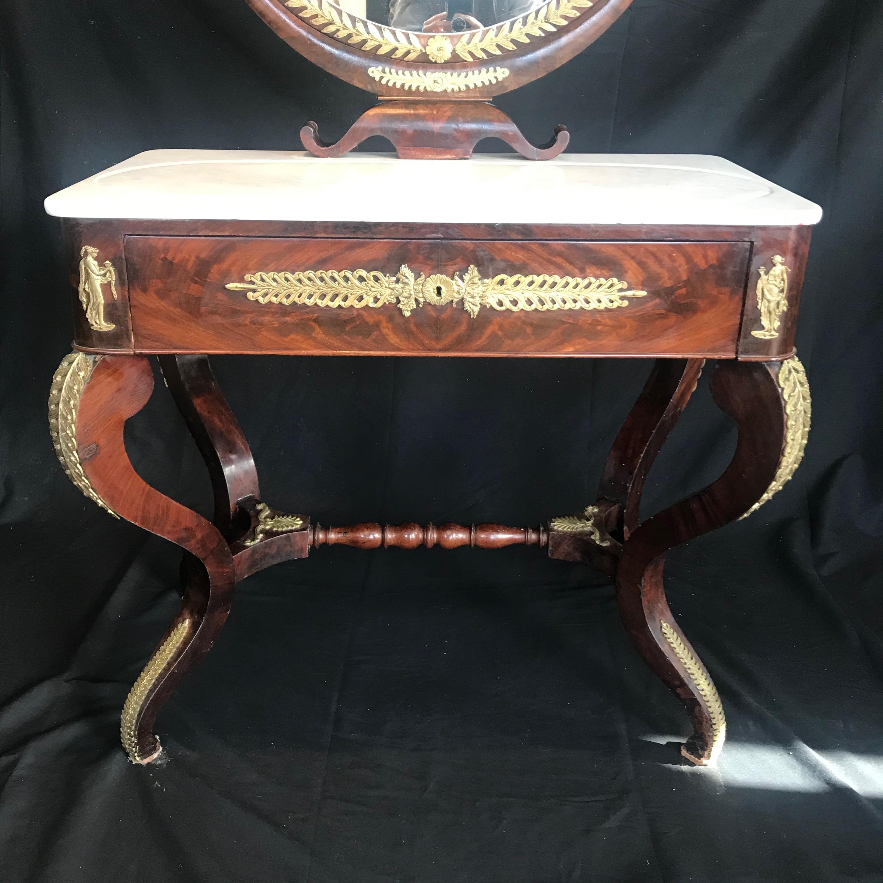 This exceptional French 19th century Empire mahogany dressing table is complete with its original mercury glass mirror and white Carrara marble top. The oval mirror is framed with beautiful brass trim and supported by mahogany carved arms in the