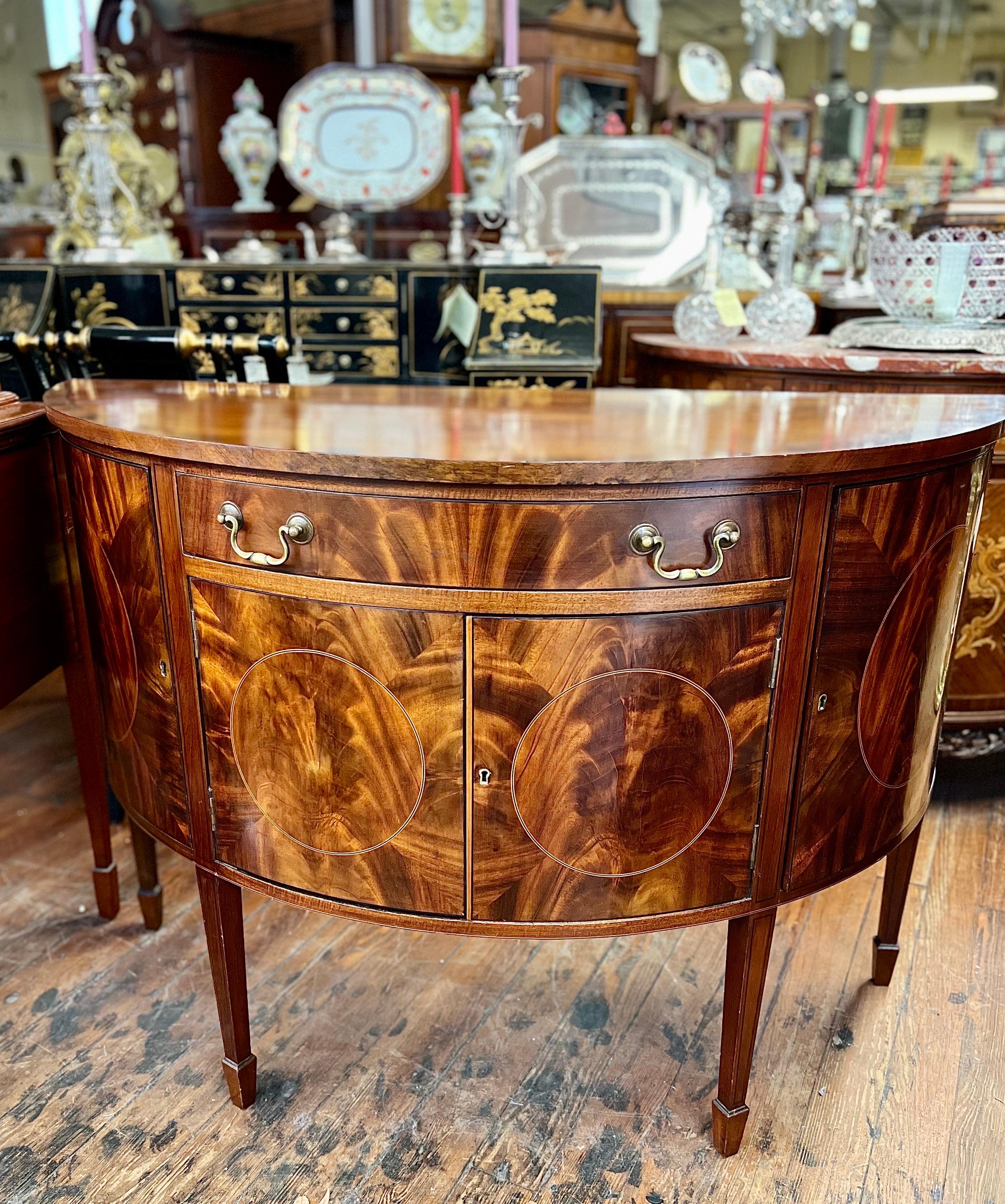 This wonderful late 19th Century English demilune Sideboard, Server or Commode has some of the most fabulous book-matched flame or crotch mahogany veneers along the front of the cupboards and drawer.  The top is solid mahogany which is crossbanded