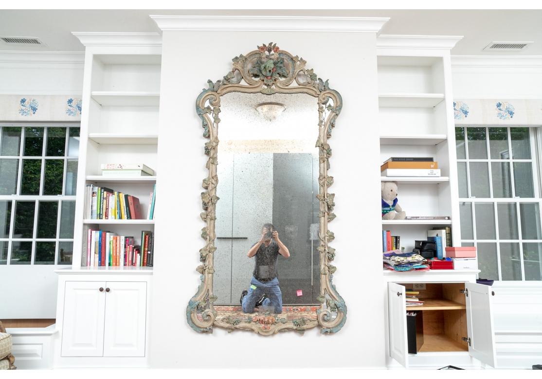 A large and very decorative Antique Mirror with hand-carved Flowers, Grape Vines with Leaves and Grape Clusters which fully surround the frame. the Mirror Crest is an ornate cluster with Leaves and Flowers framed by Scrolled  and Carved elements.