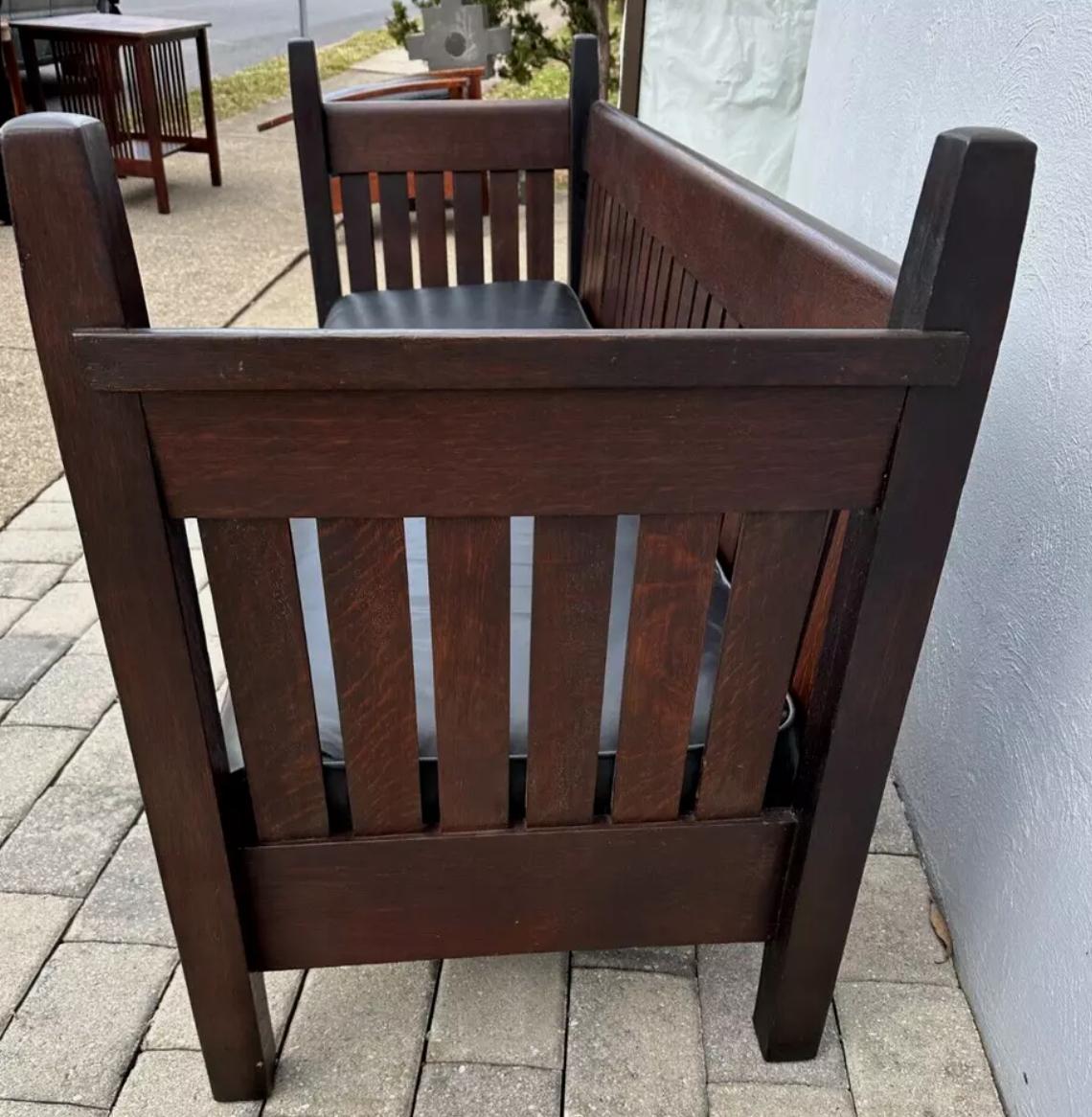 This is a great looking Gustav Stickley even arm settle (Model #222) in great condition. The settle is tall tapered post and 22 slats to back with 6 slats under each arm. The piece is in excellent original finish, with missing parts. The seat has