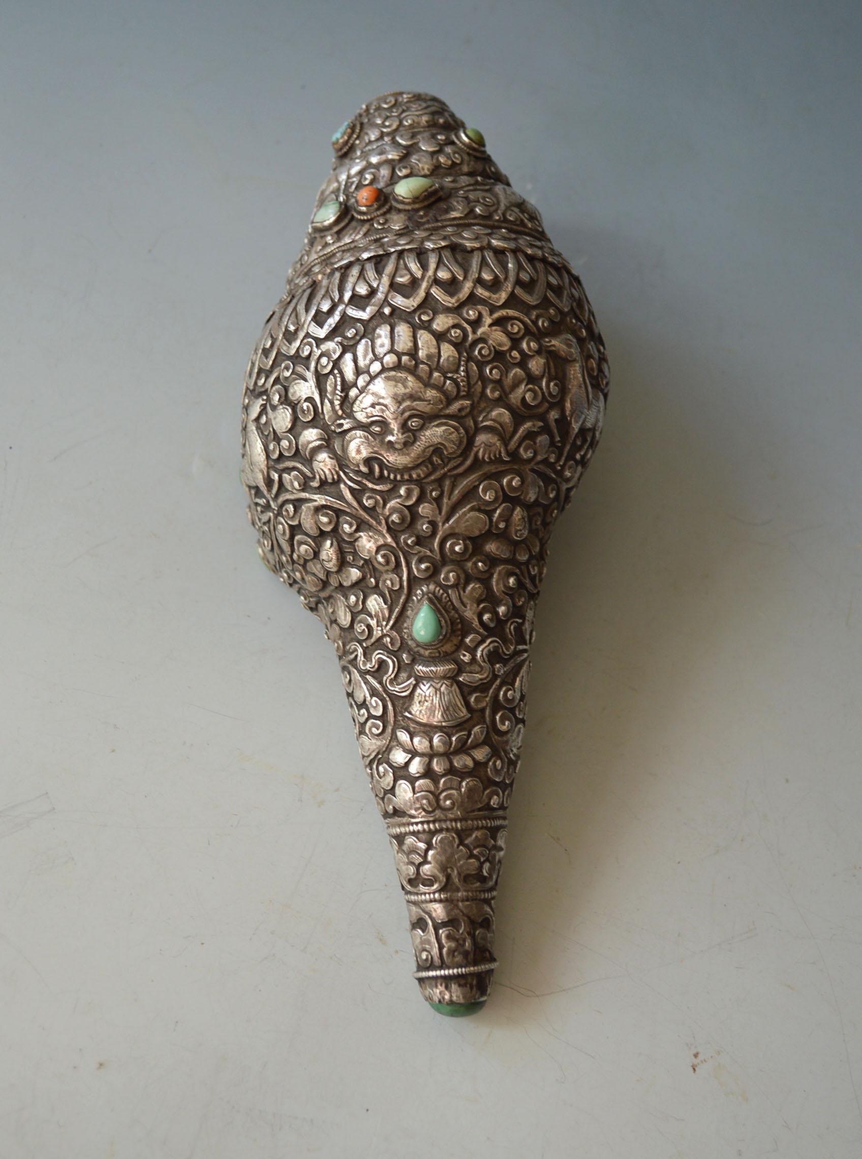 A superb Tibetan Ritual Conch covered in sliver with intricate repousse and chased floral scroll work designs featuring mythic animal with Coral Turquoise insets .
A ritual conch trumpets are considered powerful object in Tibetan Buddhism, used to