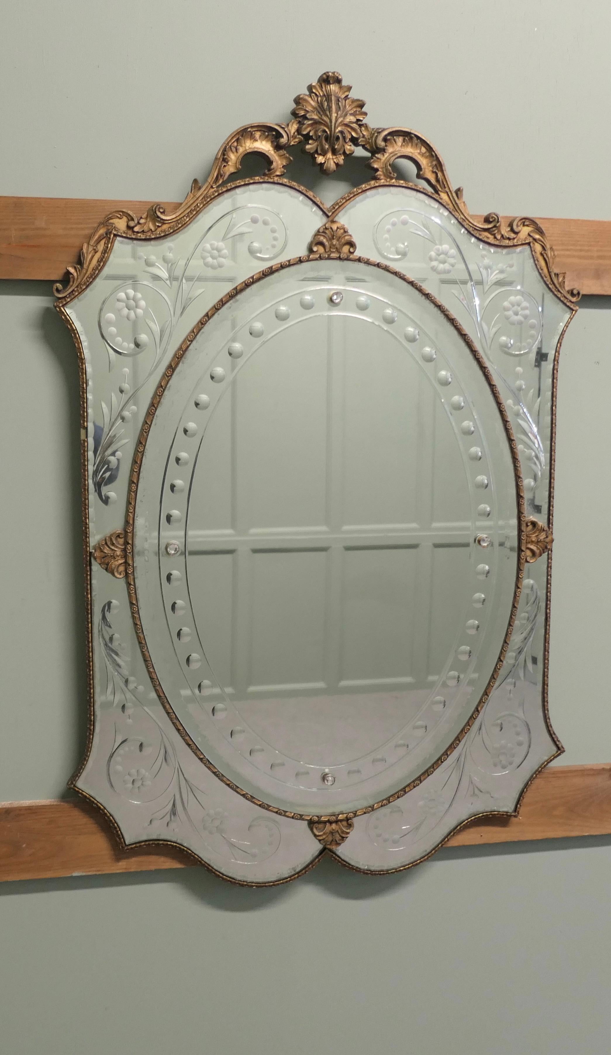 Superb Art Deco Venetian Style Mirror

This is a very attractive piece, the mirror has 5 individual etched mirrors set in a shield formation, the decorative theme carries through on the gilt gesso of the frame 
The Mirror is in very good vintage
