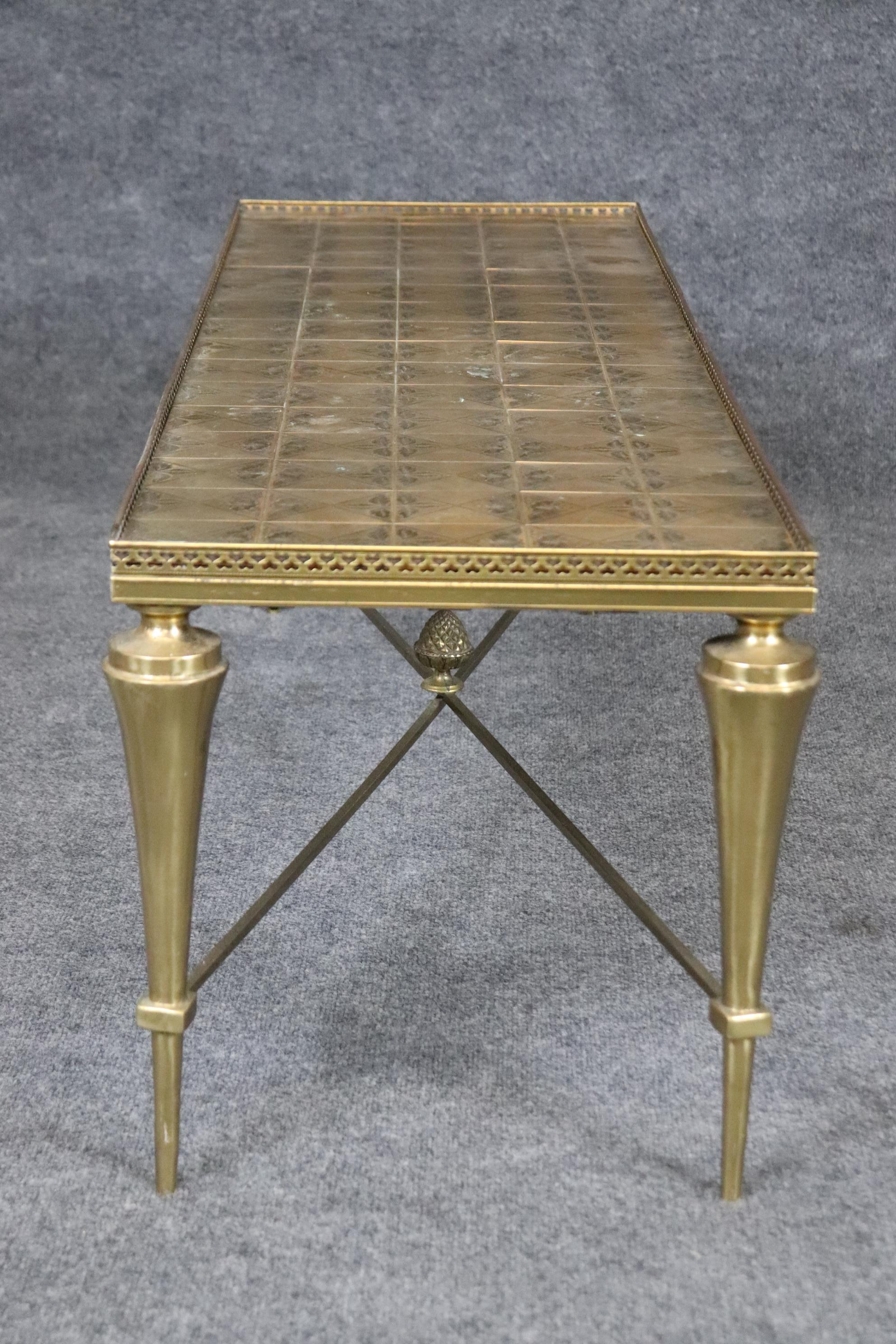 This is a Maison Jansen attributed coffee table of fine design and form made of brass in the Directoire manner. The table is in good condition and features robust conical legs and a cross stretcher with a pineapple finial and a floral designed top.
