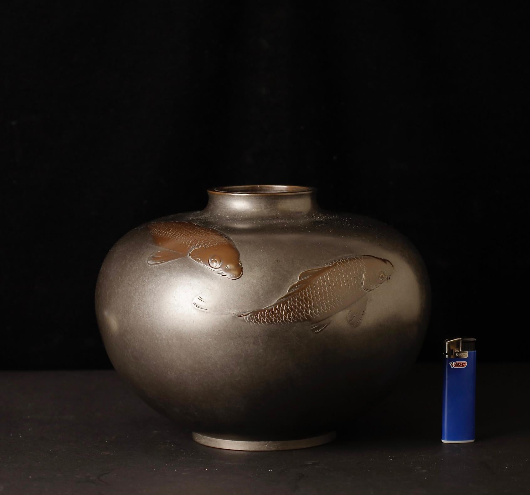 A stunning collaboration between two accomplished Japanese metal artists, this elegant bronze vase features a pair of exquisitely carved koi fish, symbolizing perseverance, transformation, and good fortune in Japanese culture. The carving, executed