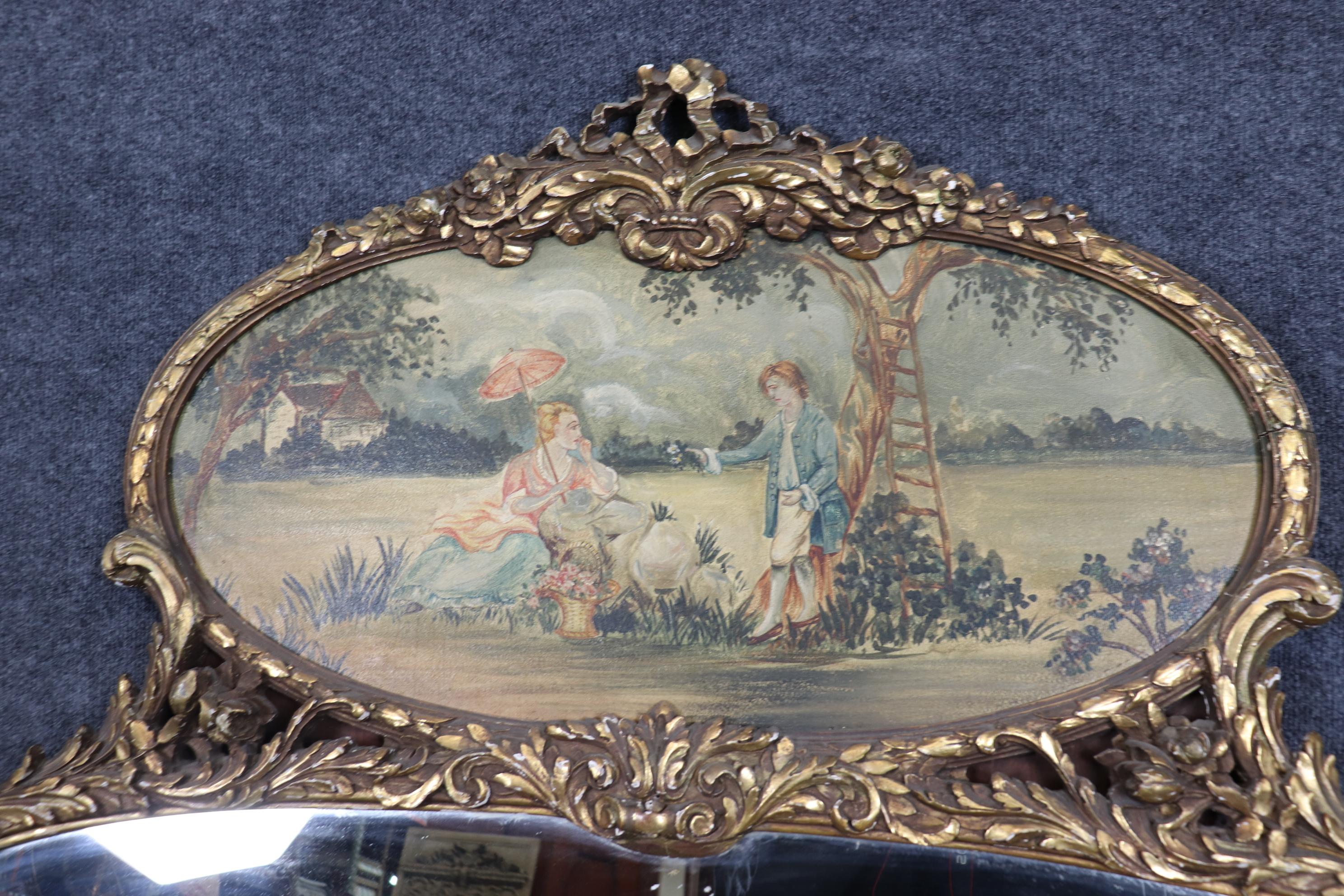 This is a gorgeous French trumeau mirror with a painted scene of courtship between two lovers all dressed up with their best finery and a parasol. The mirror is beautifully gilded and is in good condition with no damage and a beautiful painted scene