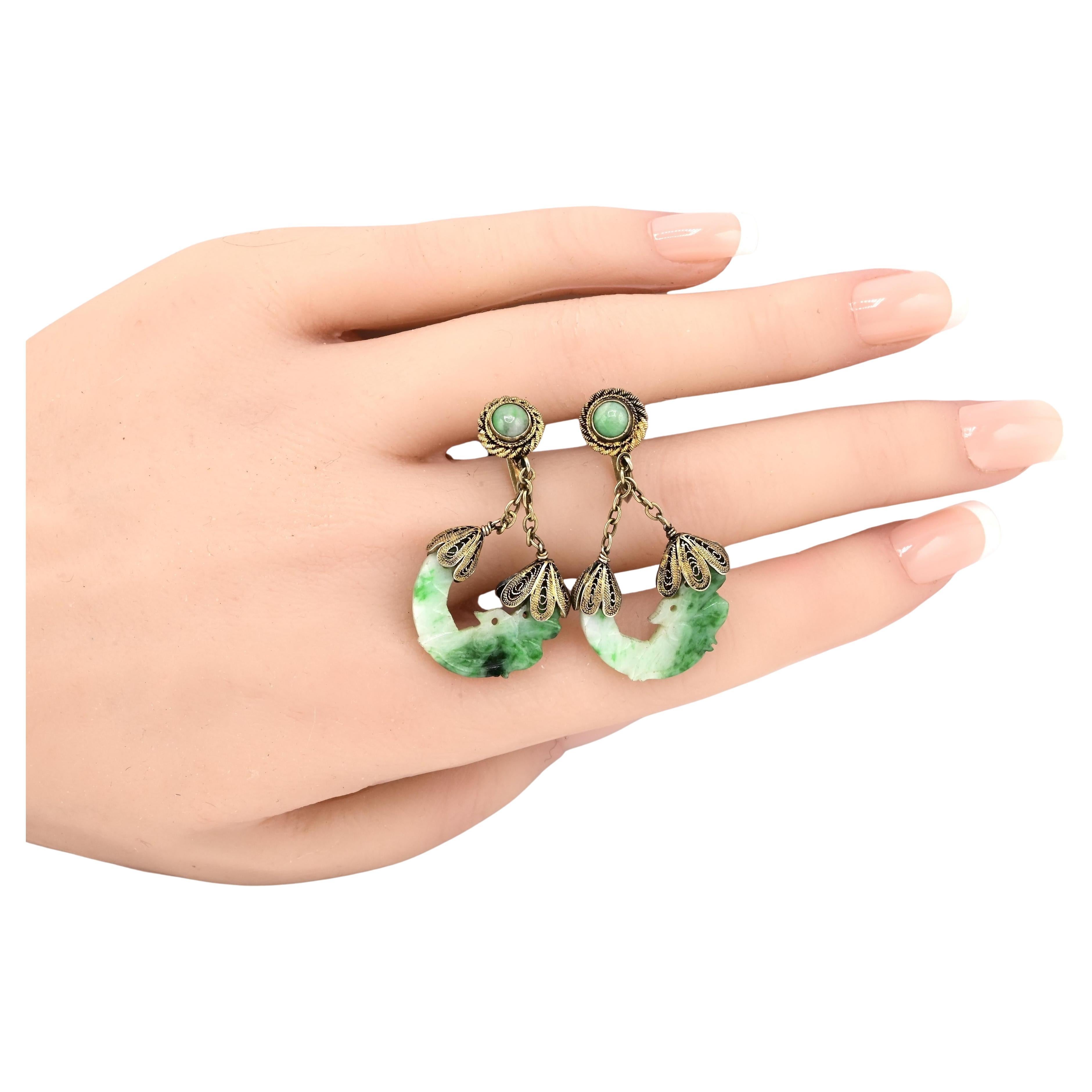 These vintage earrings are a captivating piece of jewelry. Crafted with intricate silver metalwork, they feature a delicate filigree design. The earrings showcase green jade accents, adding a touch of elegance. The dangling elements are shaped like