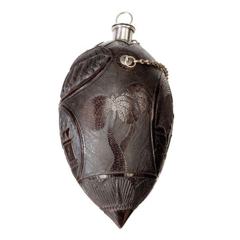 A superb coconut shell “bugbear” powder flask with silver mounts and carrying chain (France, circa 1790)
the top finely carved with a native face with curled hair and inlaid eyes, the mouth with a stopper on a chain, the central frieze with ovals