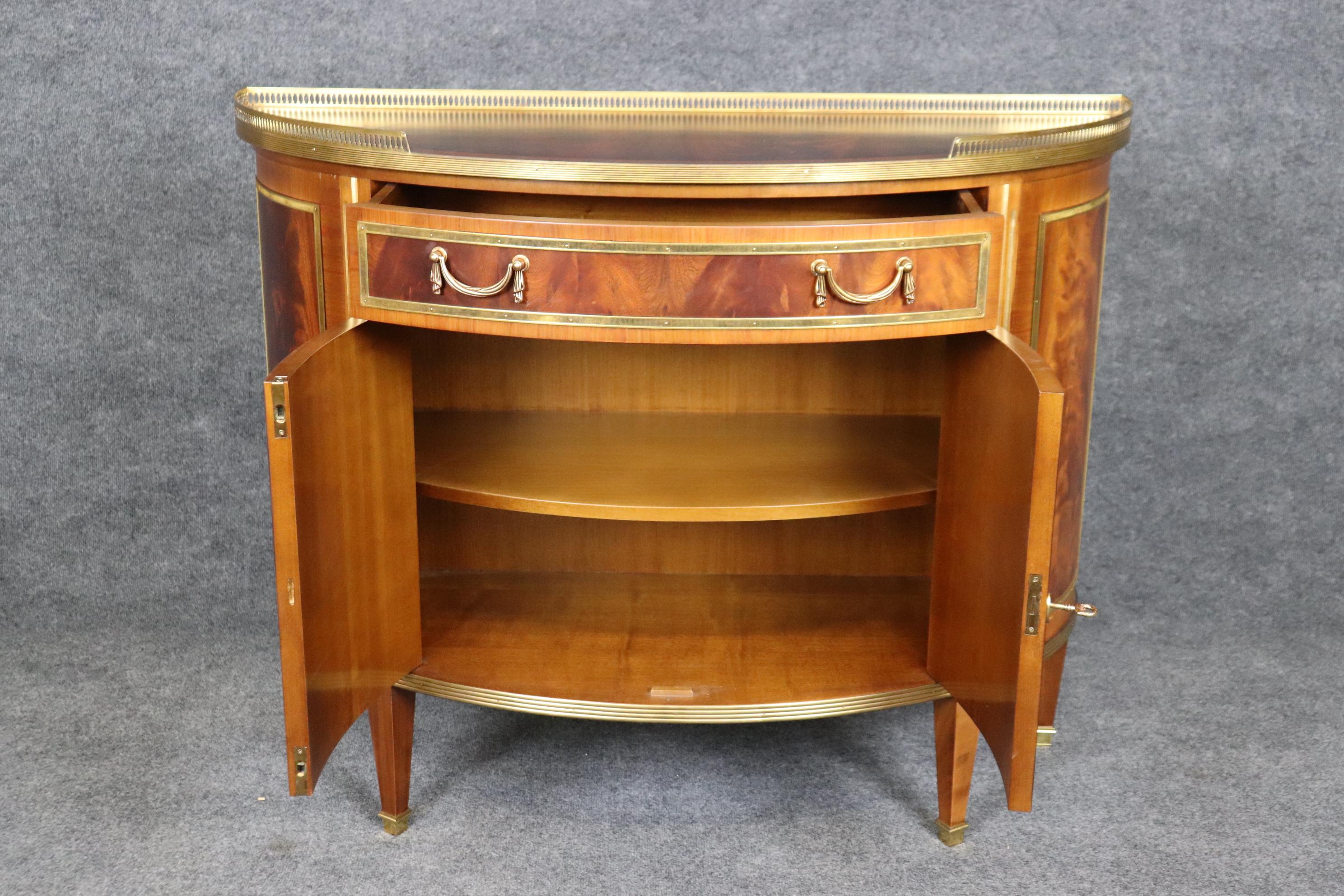 This is a superb Decorative Crafts Italian-made flame mahogany bronze and brass adorned demilune Louis XVI or Directoire commode. The quality is breathtaking and this is a in good condition as it is not that old. The piece is a masterpiece and will