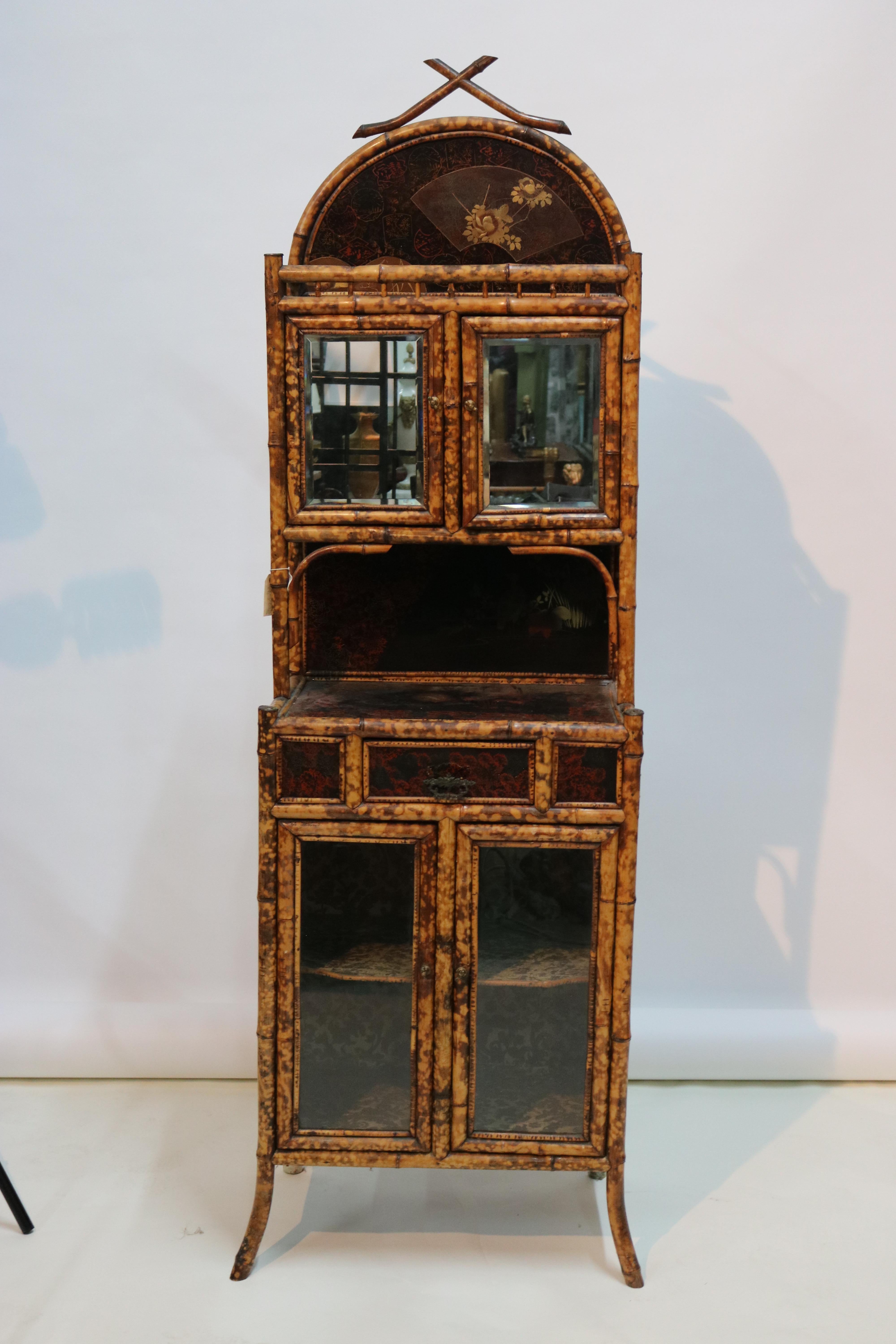 A large 1880s English bamboo cabinet featuring an upper tier with an Aesthetic Movement design of lacquered panels and fretwork with a pair of rectangular beveled mirrored doors with interior shelf,, over a cabinet lower tier with fine Japan