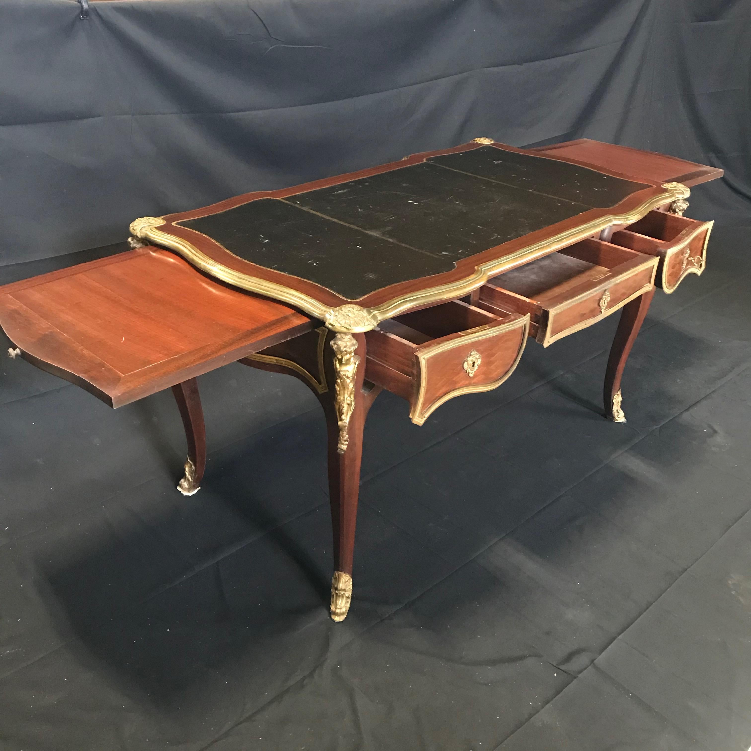 A very fine French 19th century Louis XV style ormolu-mounted mahogany and
kingwood three-drawer bureau plat having a rectangular curvy shaped top that frames
a handsome tooled black leather writing surface. There are molded borders above
three