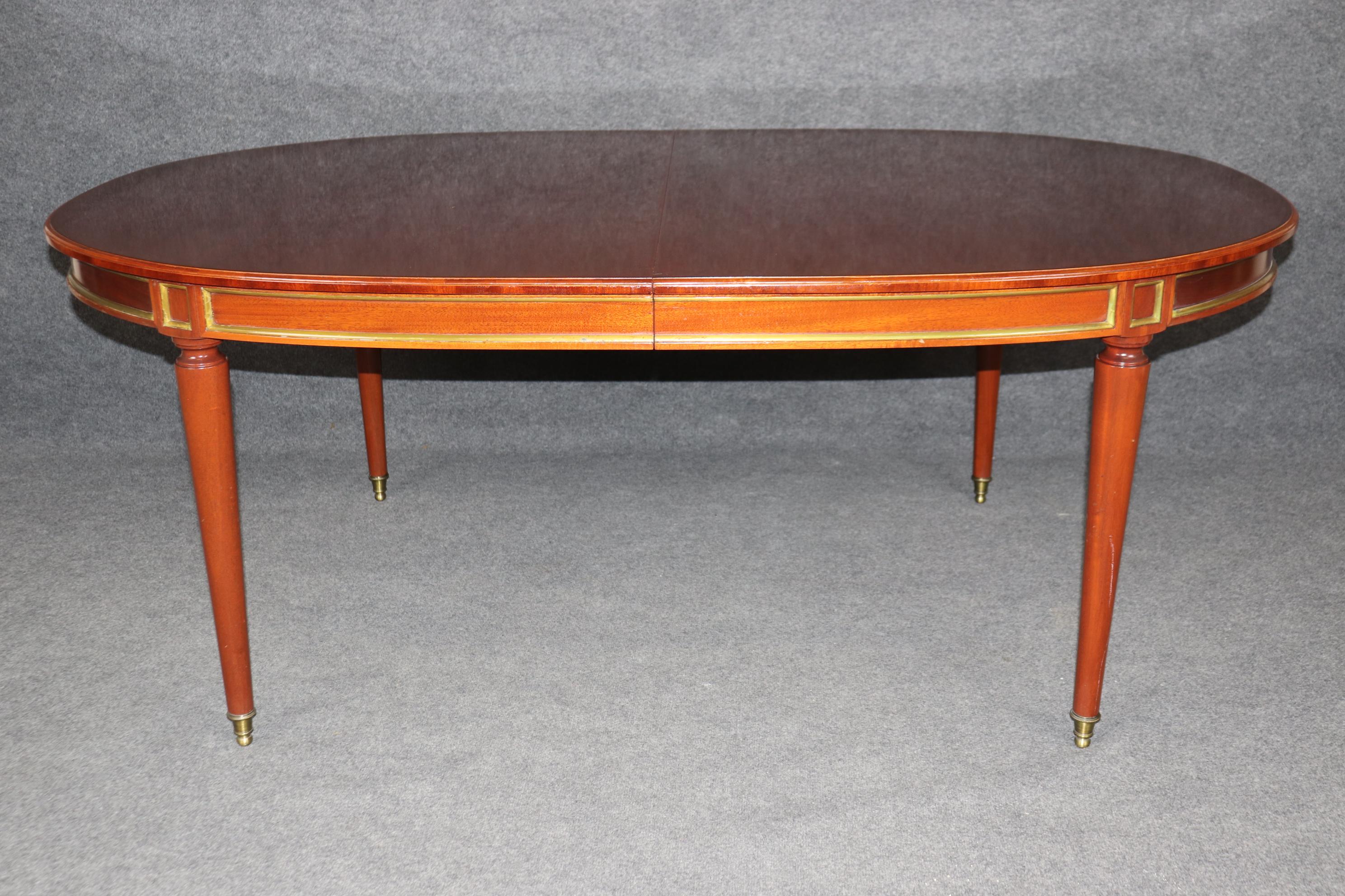 Il s'agit d'une table de salle à manger à la fois simple et chic avec deux feuilles de 24 pouces. La table a été fabriquée en France, comme l'indique le cachet apposé sous les pieds en laiton. La table est en bon état et présente des signes mineurs
