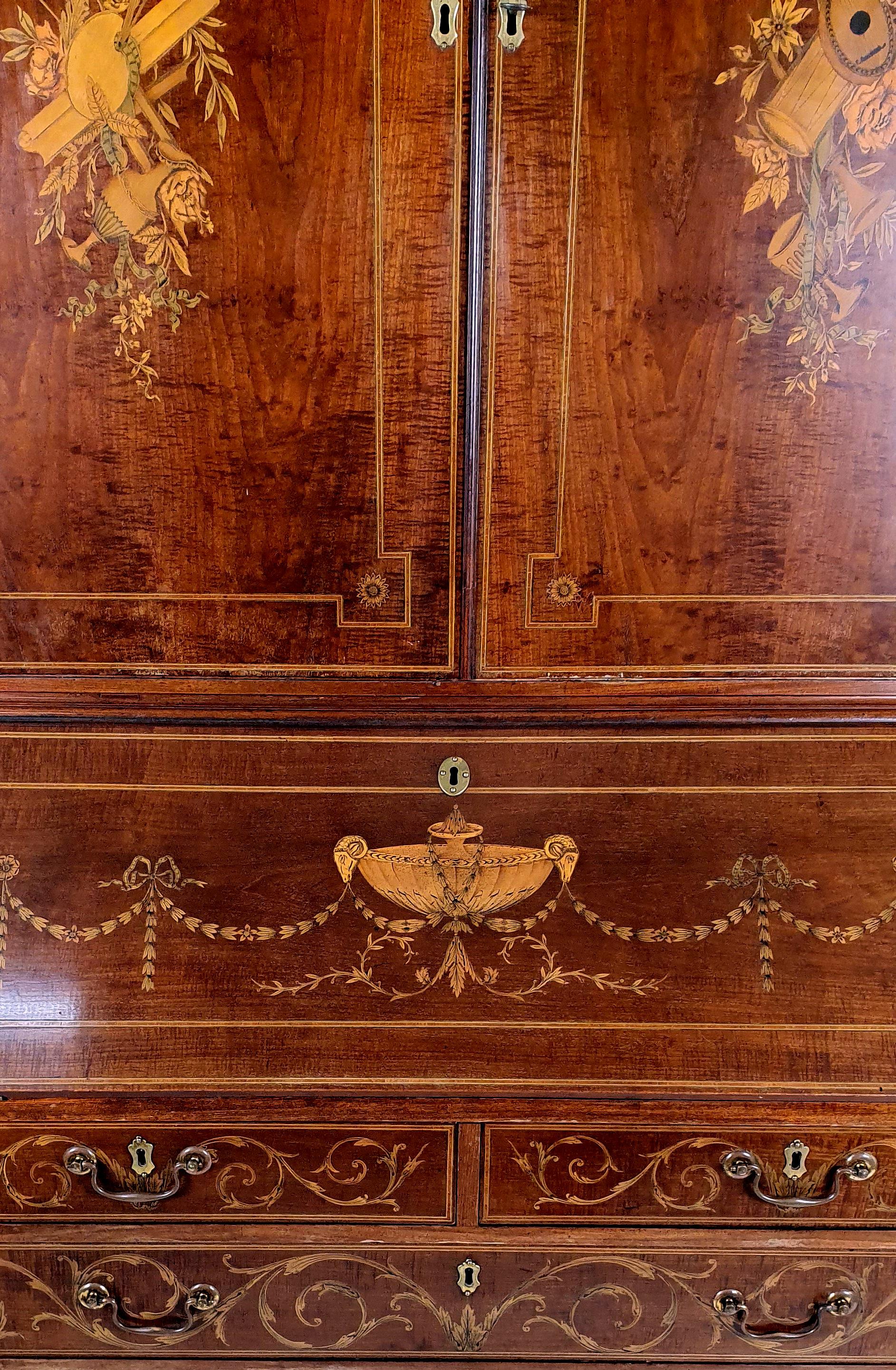 This superb and ornately detailed George III mahogany bureau bookcase is decorated with swags, musical instruments and rams heads inlaid with satinwood. The top section has 3 fully adjustable shelves with a central drop down writing desk top