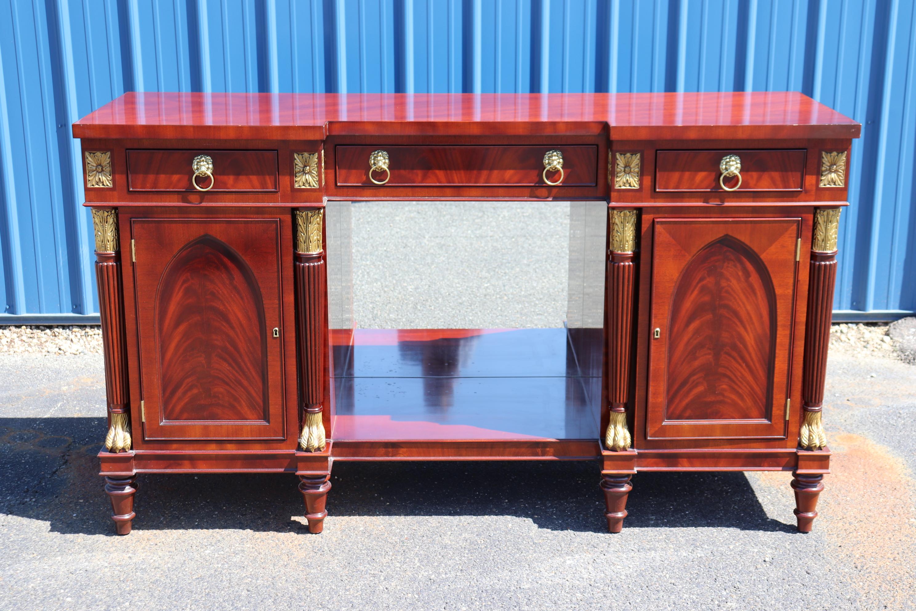 This is a beautiful Kindel furniture sideboard from the Winterthur Adaptations collection. This piece features gothic paneled flame mahogany doors and gorgeous gold leaf and has a mirrored interior inside the bottom. The sideboard is in good