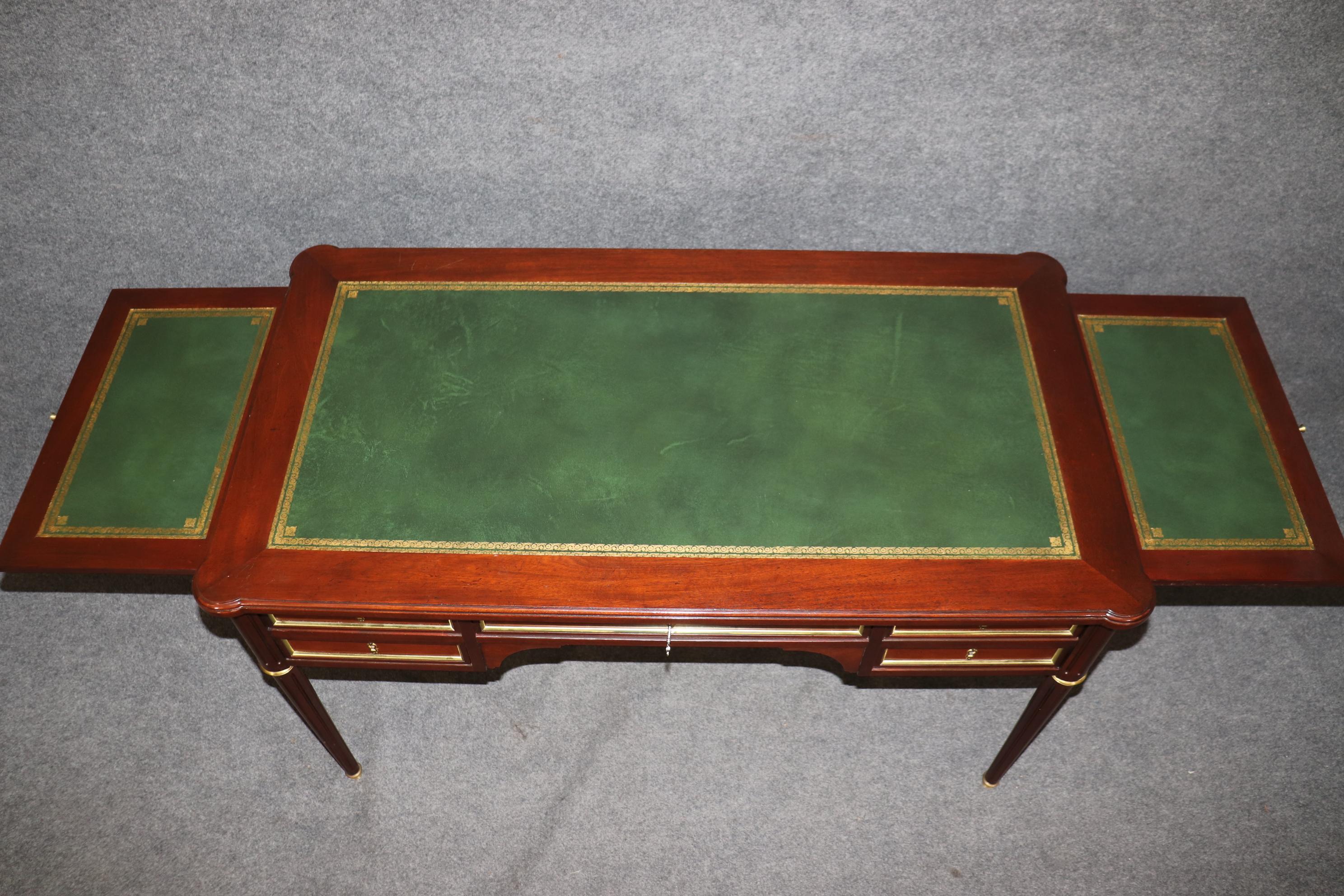 This is a gorgeous Baker Desk in the French Directoire style. The desk is beautifully made of mahogany with bright brass trim and a beautiful leather top with gold tooled embossing and pull out leather tablet trays for additional working space. The