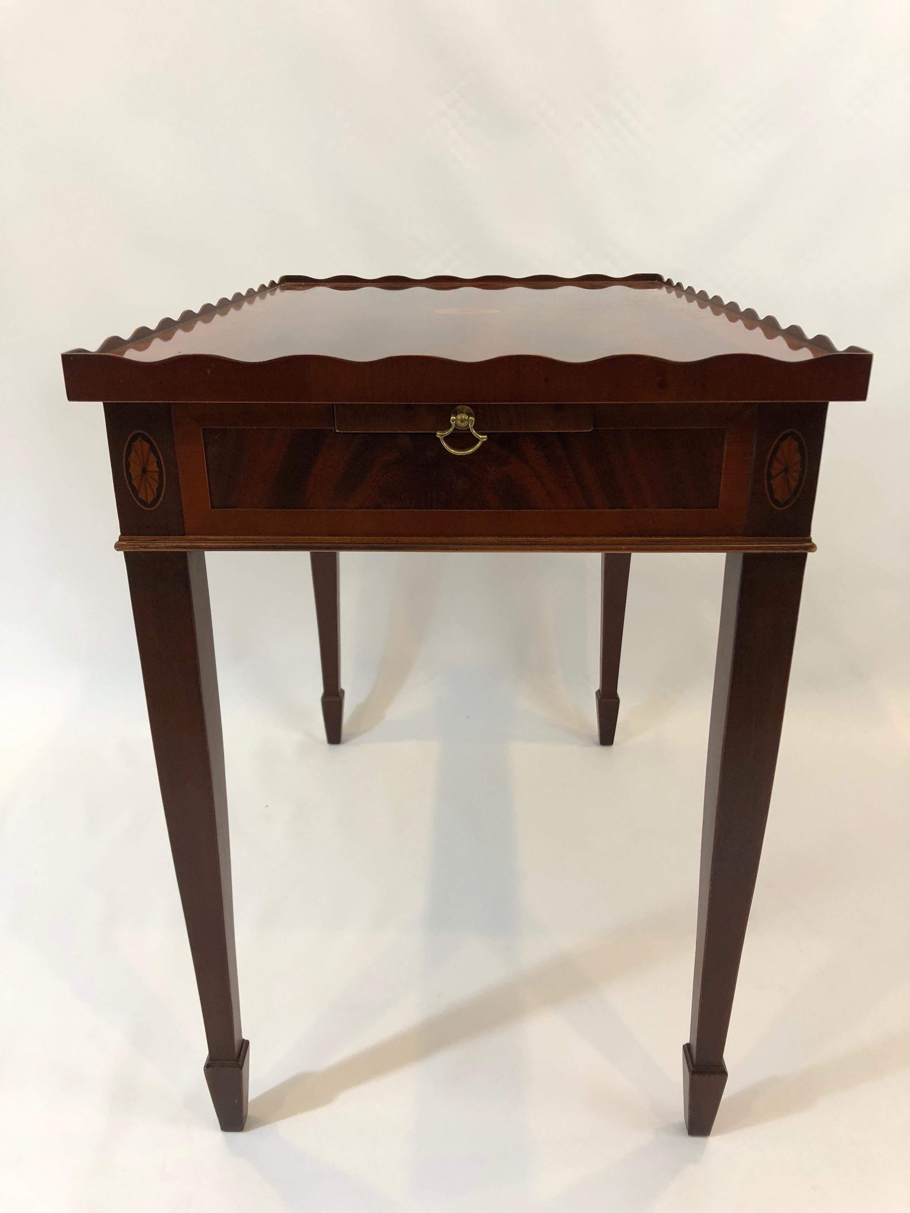An elegant flame mahogany tea table by Heckman having a pretty scalloped pie crust edge, satinwood and ebony fan inlay, and two slides that pull out at each end.
