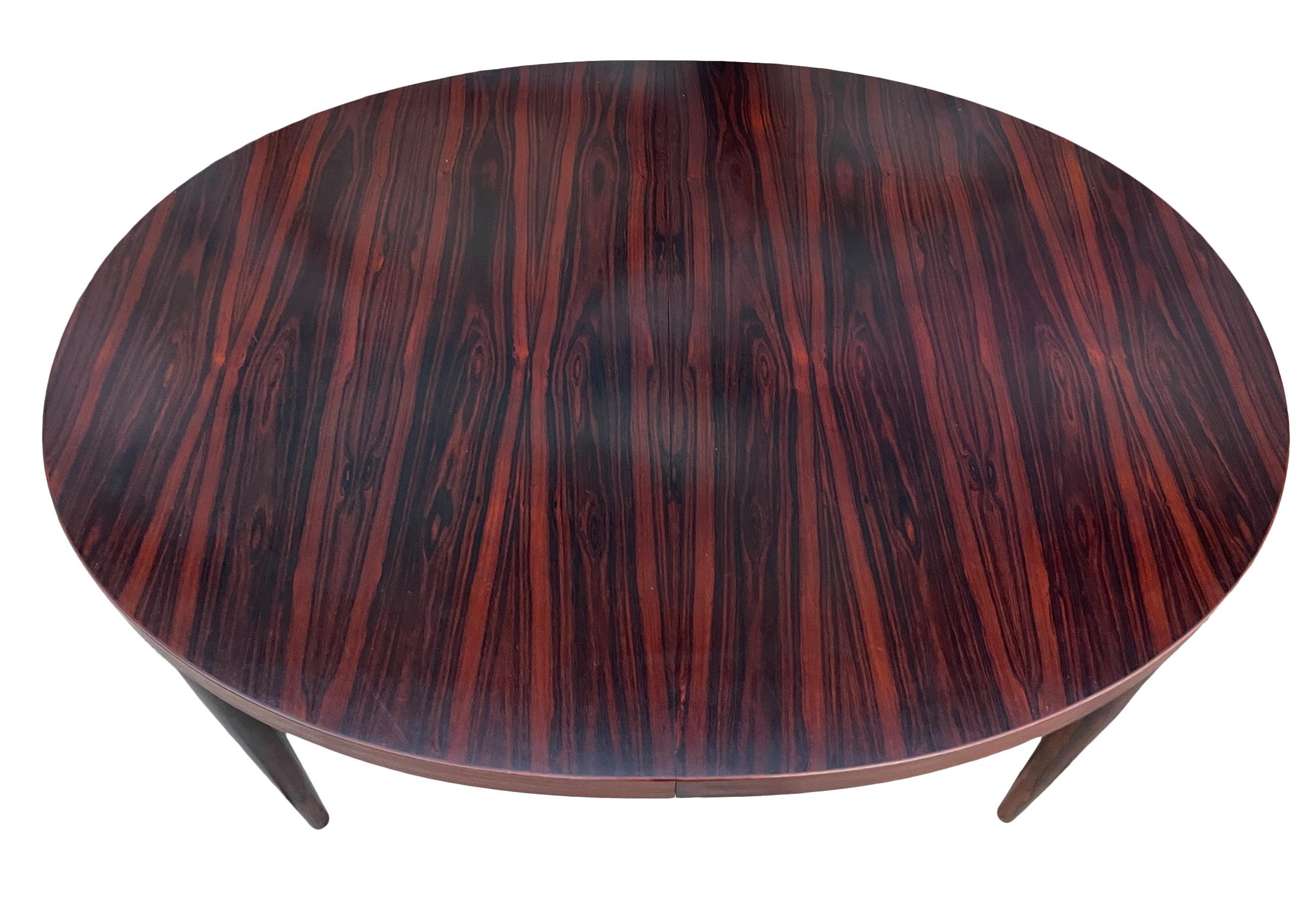 Stunning Mid century Exotic rosewood oval Danish Modern extension dining table with (2) leaves. This table has Solid rosewood tapered wood legs. This table is in beautiful condition with Dark black and reddish rosewood tones very Magical Table.