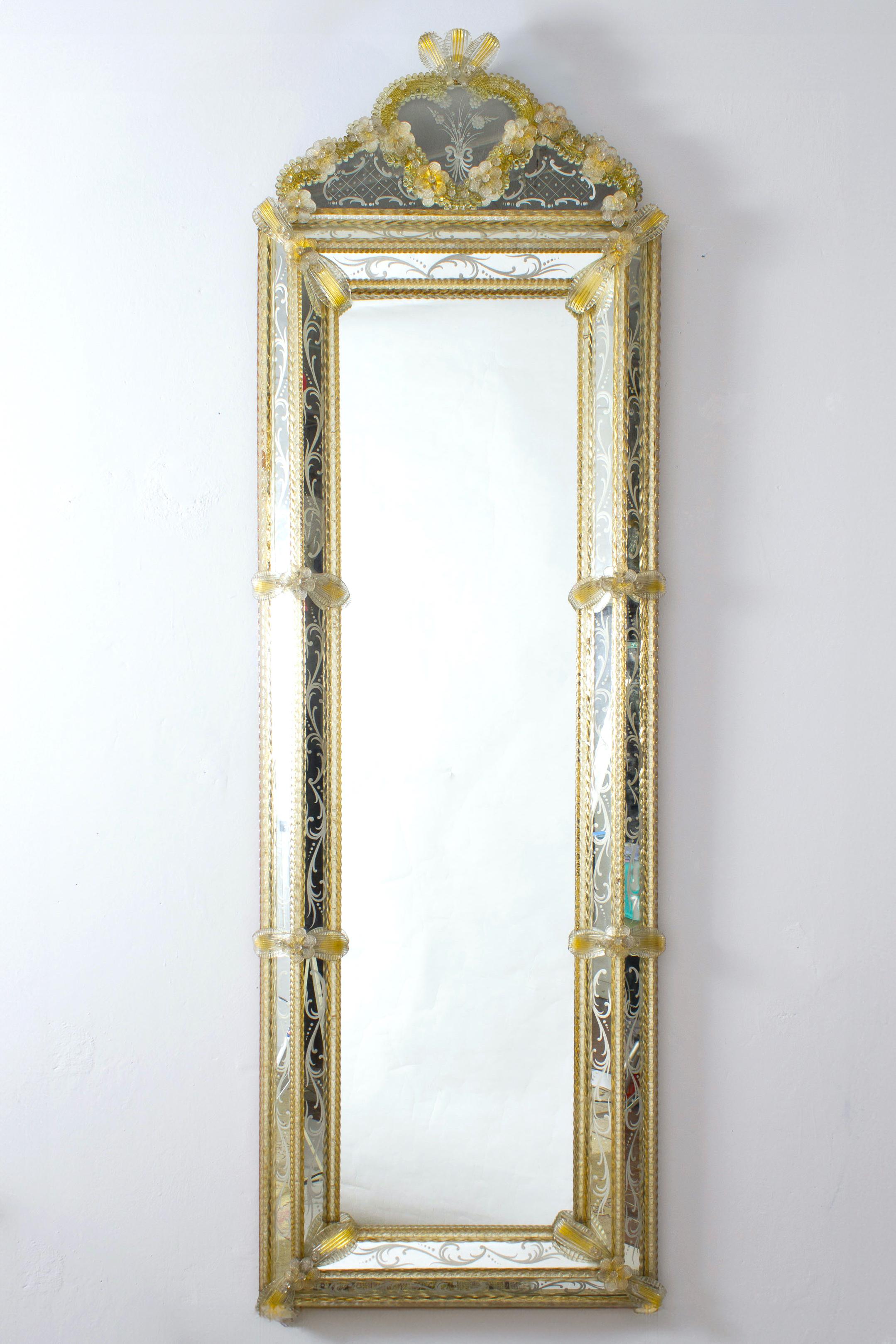 Ce magnifique miroir vénitien présente des motifs floraux gravés qui ornent le cadre du miroir. Le long des bords du cadre se trouvent des accents de corde en verre doré et de nombreuses fleurs en verre. 
Excellent état vintage.