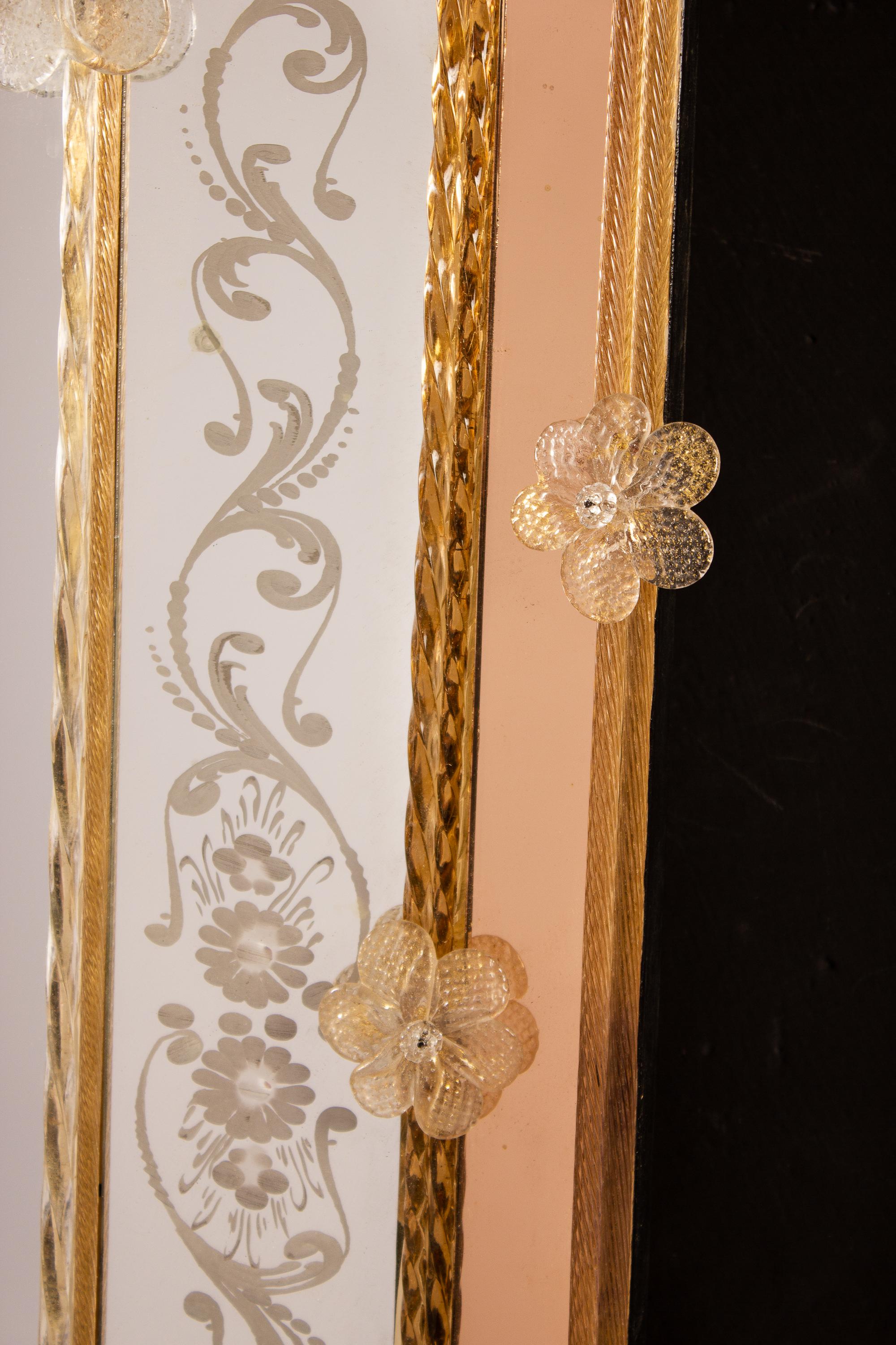 This beautiful Venetian mirror features etched floral motifs adorning the mirrored frame. Along the edges of the frame are glass rope accents and numerous glass gold flowers. Executed by the great Master of Murano Oscar Zanetti. 
The mirror is
