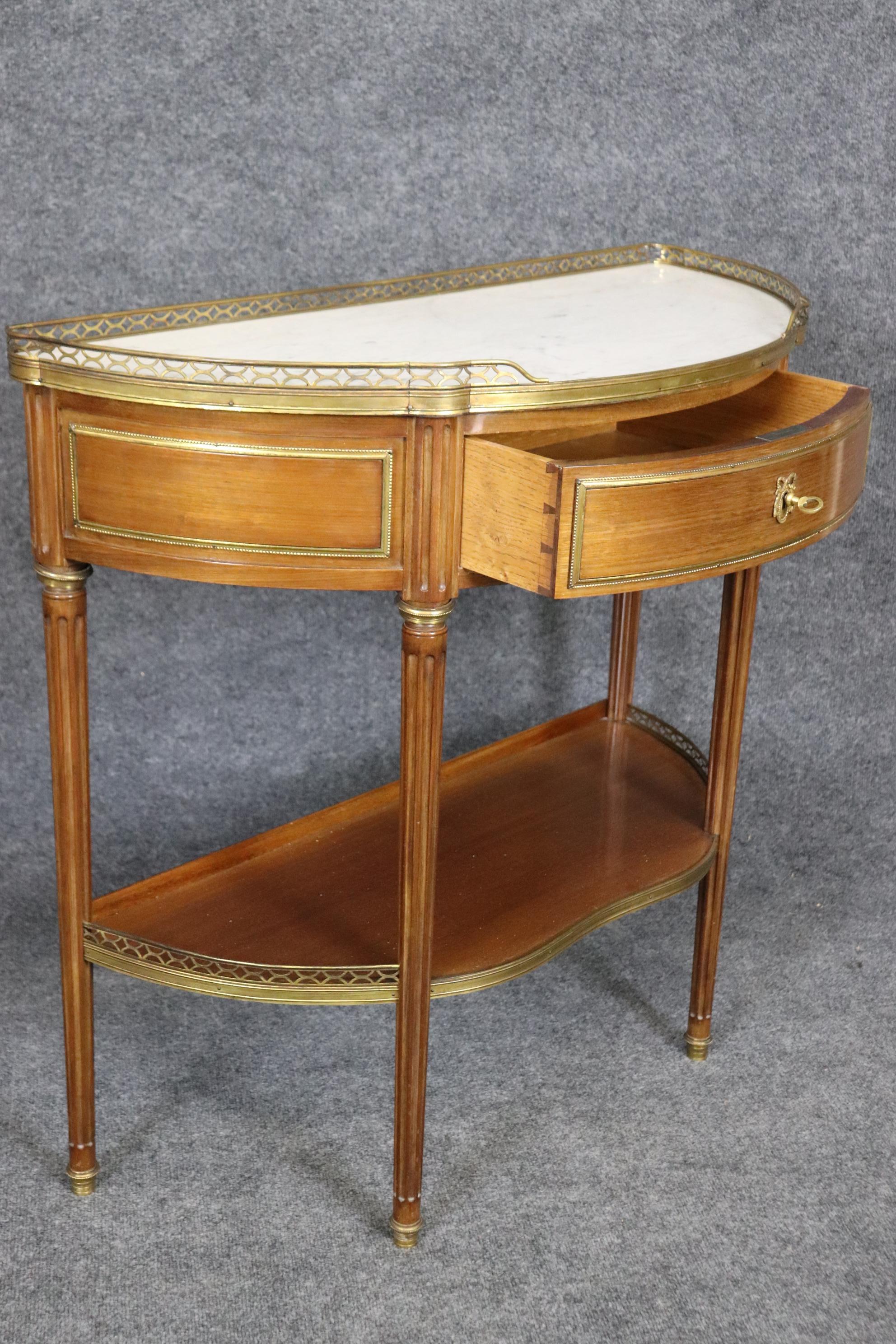 This is a fantastic pair of demilune tables made in France of walnut with groegous brass and bronze ormolu. The tables feature beautiful wood quality and brass and bronze. The tables have white marble tops and are in good condition for their age.
