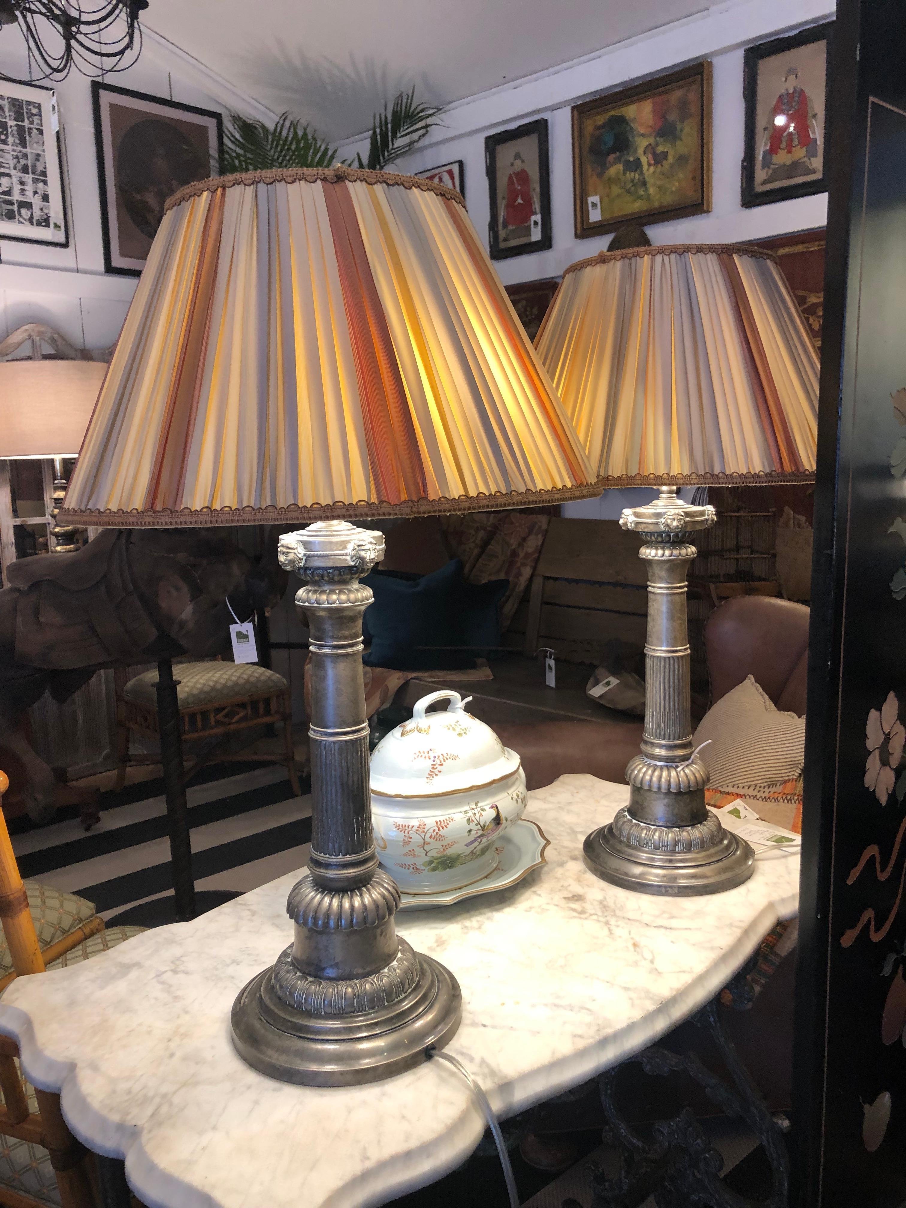 Magnificent pair of pewter silverplate corinthian column neoclassical lamps .   having lion heads detailing near top of each column and amazing hand made silk pleated shades in warm earth tones. 