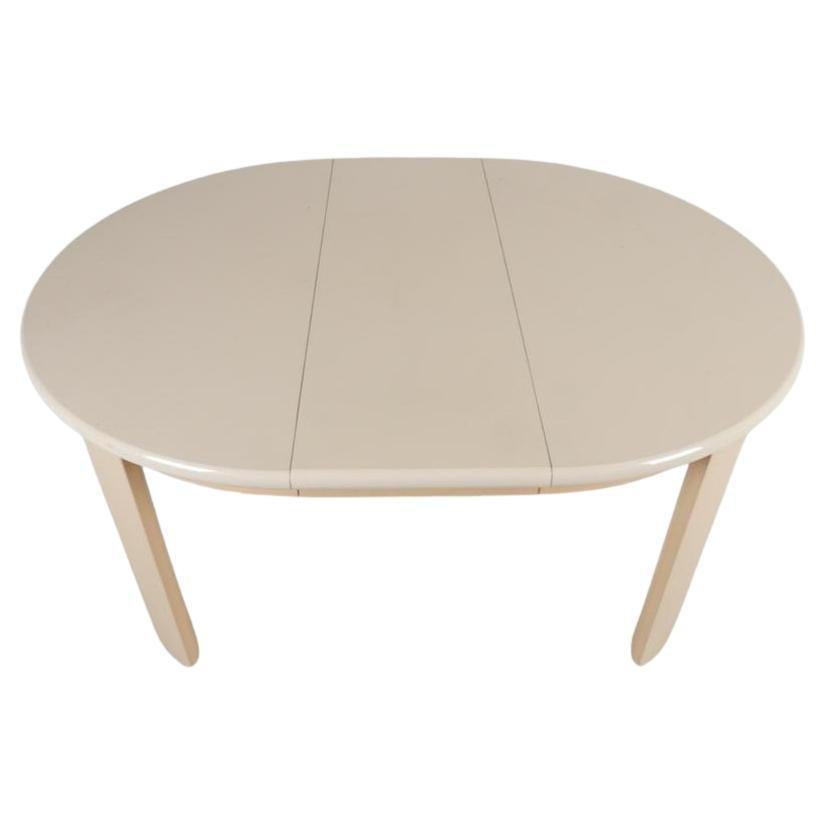 Post modern gloss lacquer tan round dining table with 1 leaf. Taupe gloss Lacquered expanding oval dining table with one leaf that seats 4-6 chairs. Has curved popsicle shaped legs. Apron and legs are a darker shade of tan. Very good vintage