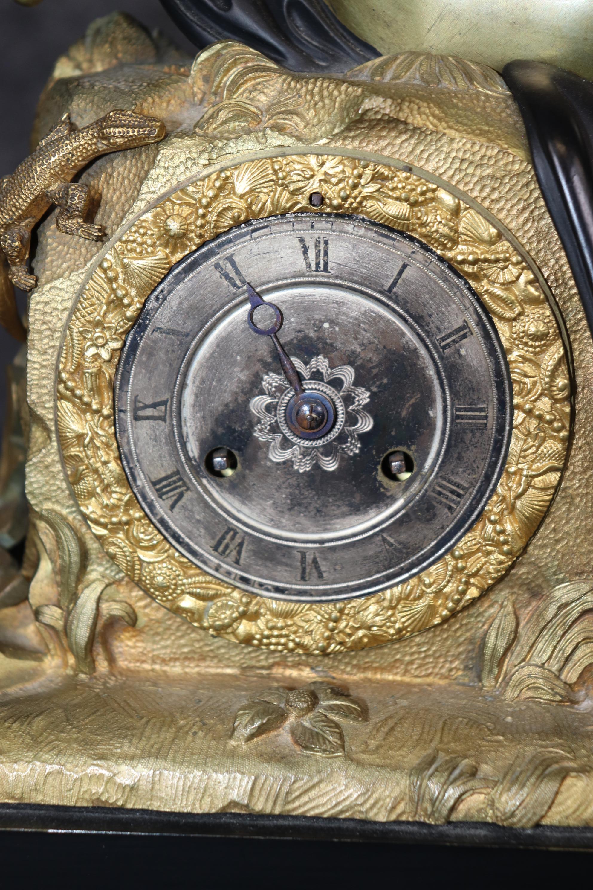 Se trata de un reloj figurativo de bronce absolutamente impresionante en el que aparecen un joven, un lagarto o geco y diversos motivos, como instrumentos musicales y otros diseños. El contraste entre la caja ebonizada y el bronce natural revela la