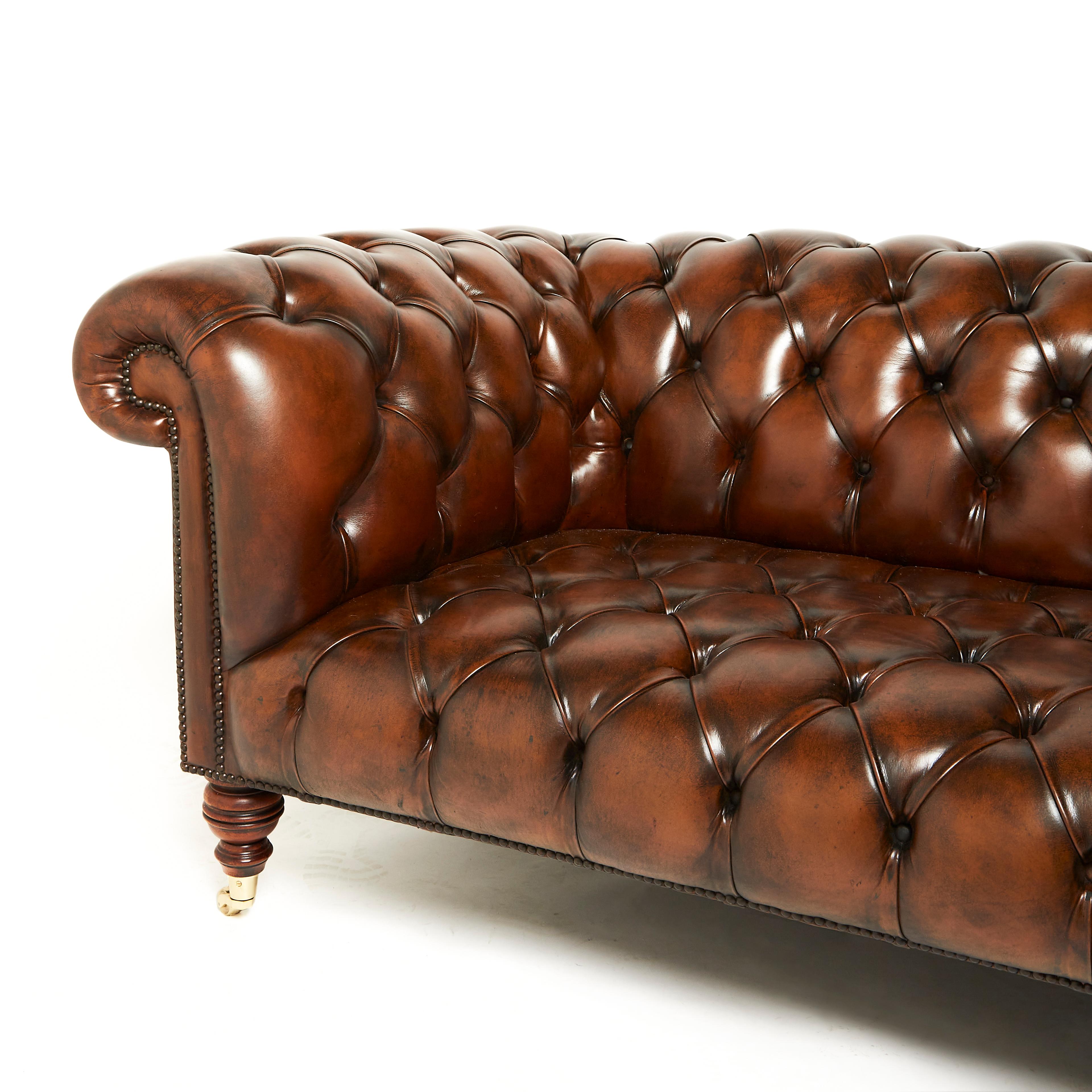 This superb quality and classic styled English chesterfield sofa features deep buttoned leather upholstery with rolled back and arm rests. The sofa is one piece with turned mahogany legs and supported on brass casters. It measures a massive 96