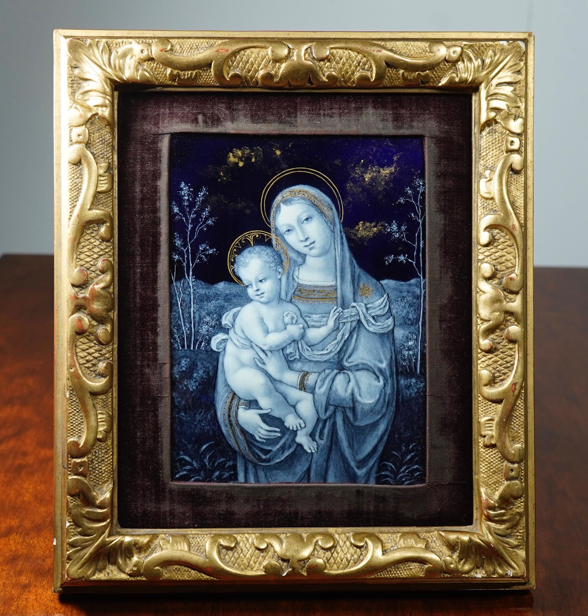 Superb French enamel plaque, painted in white enamel over a deep blue ground with a Renaissance style Madonna and Child, each outlined in halos of gold, the background wooded landscape with gilt clouds above, set in a carved giltwood frame with