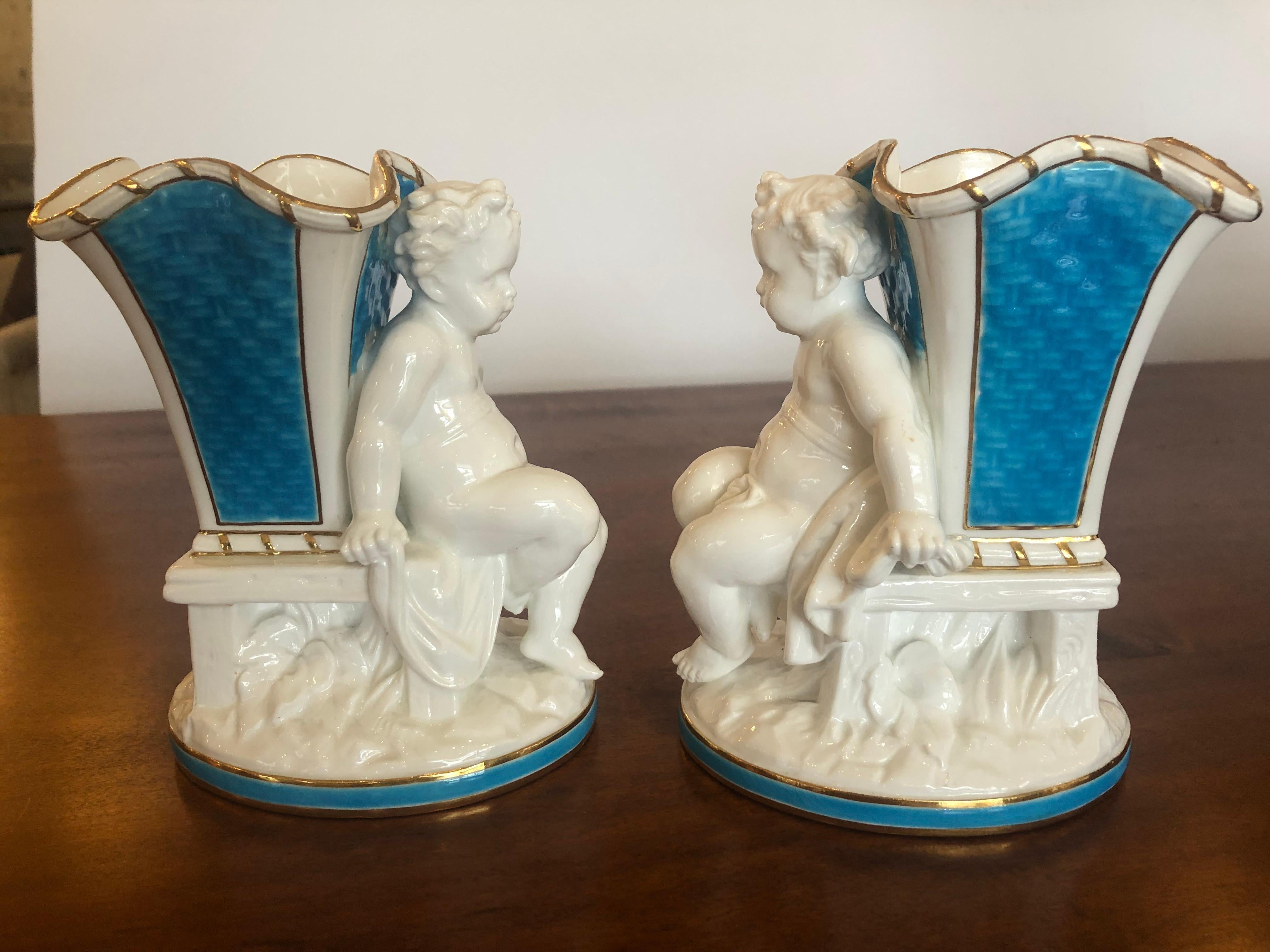 A sublime pair of porcelain spill vases having scalloped edges, gold leaf, eye catching Tiffany blue patterned decoration, and seated cherubs. Marked on bottoms, England, Caldwell & Philadelphia.
   