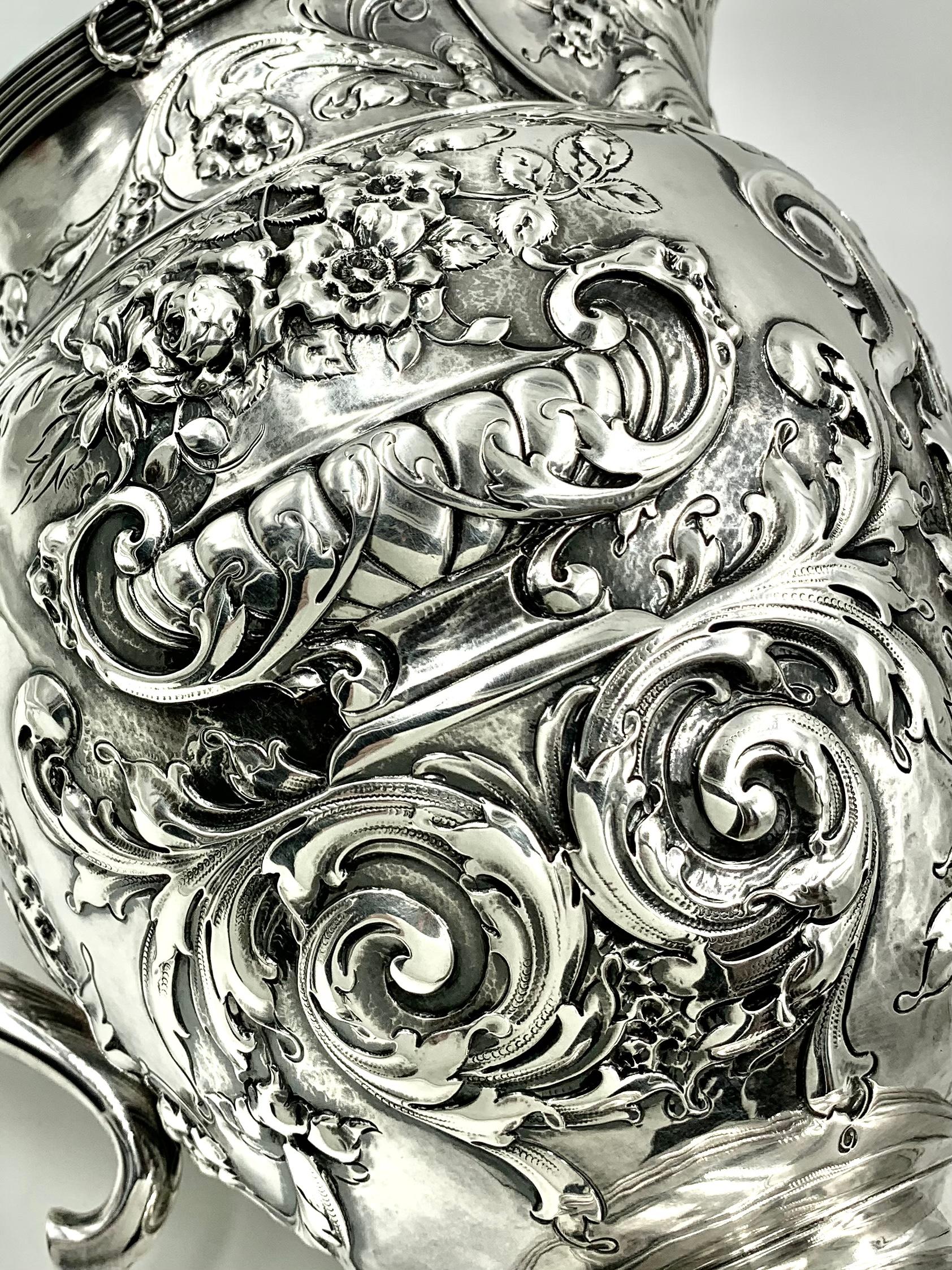 Une magnifique aiguière avec un exquis travail d'argent repoussé représentant de généreux vases Campagna débordant de fleurs, posés sur des bases feuillagées. La décoration du bord présente un motif de ruban doublé et orné de couronnes. Le motif