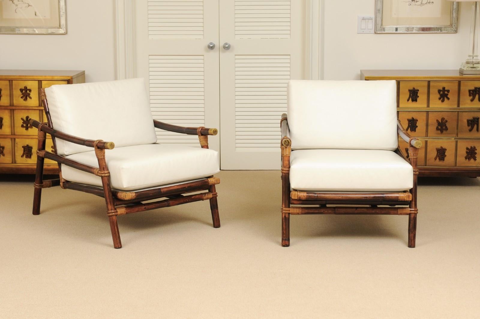 An exceptional pair of vintage Campaign style lounge chairs with matching ottoman from a difficult to find seating series. Stout rattan and hardwood frame with a beautiful raffia seat back. Handsome solid brass accents mark the arms. Fabulous