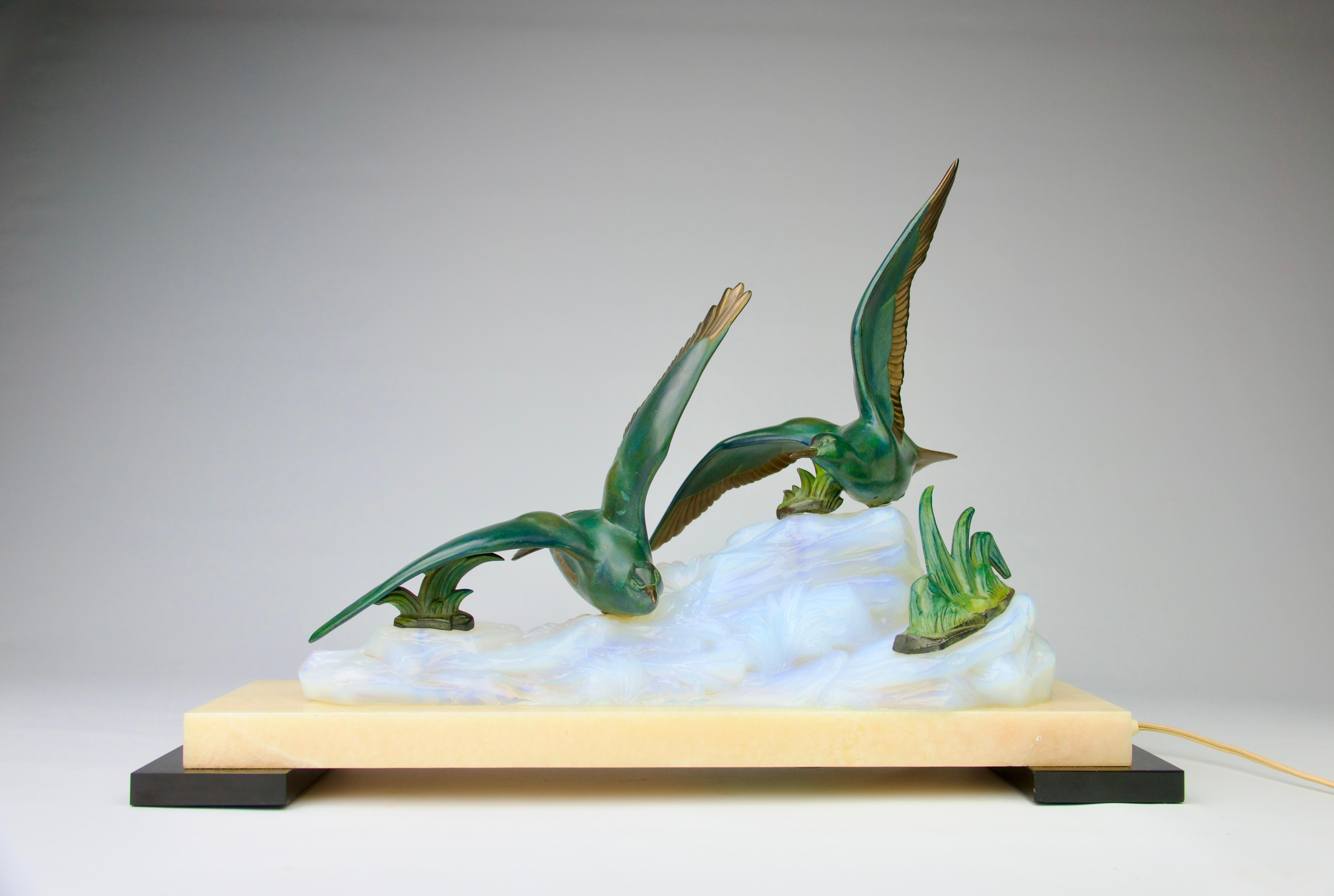 Superb art deco table lamp featuring patinated bronze seagulls flying over waves made of opalescent glass. Lighting inside the glass sitting atop a marble base of black and beige marble. 

In very good, slight signs of use.

Dimensions in cm ( H x L