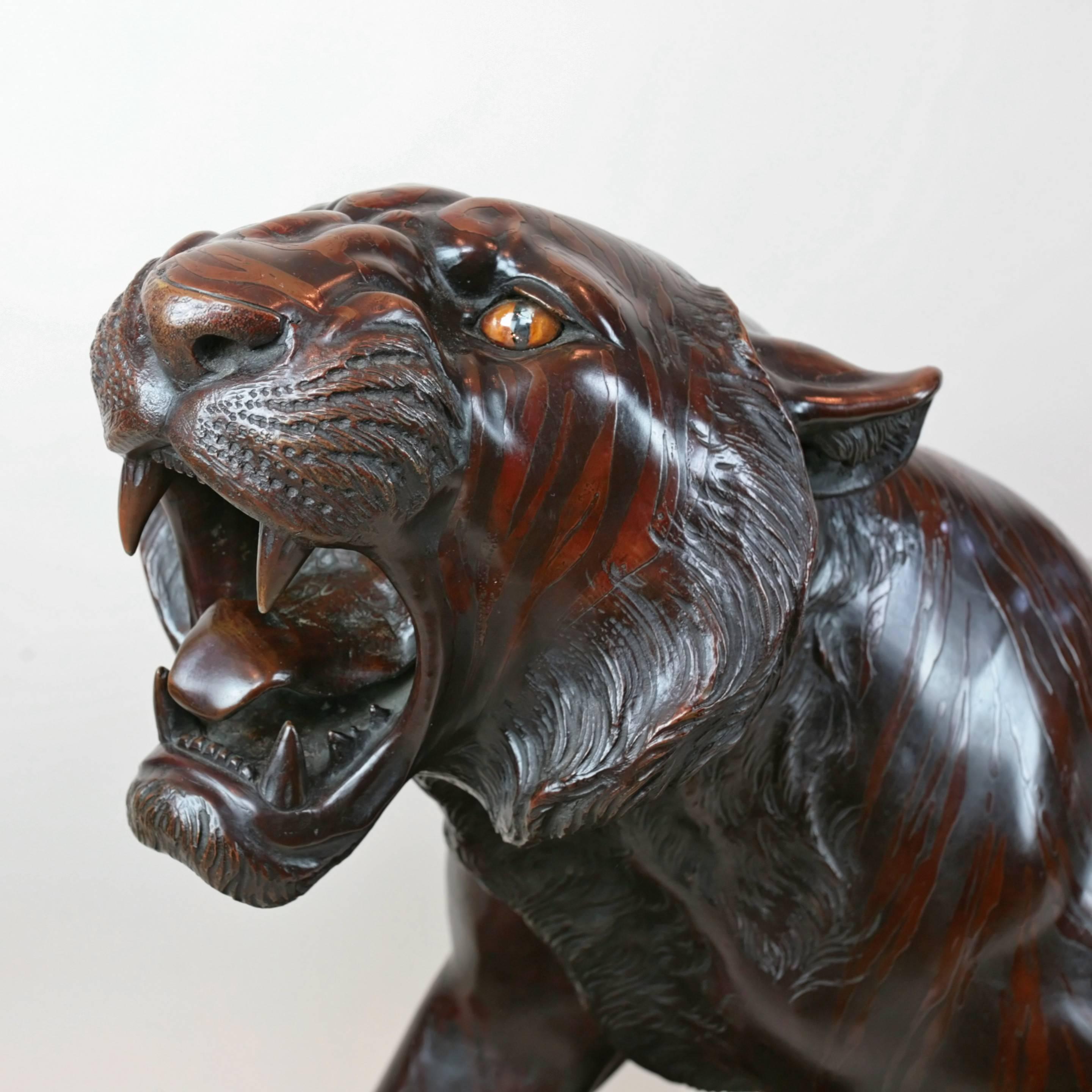 The bronze body patinated to imitate the distinctive stripes of a tiger’s skin, with inset orange glass eyes. Signed in a seal tsunematsu. On a carved hardwood base.