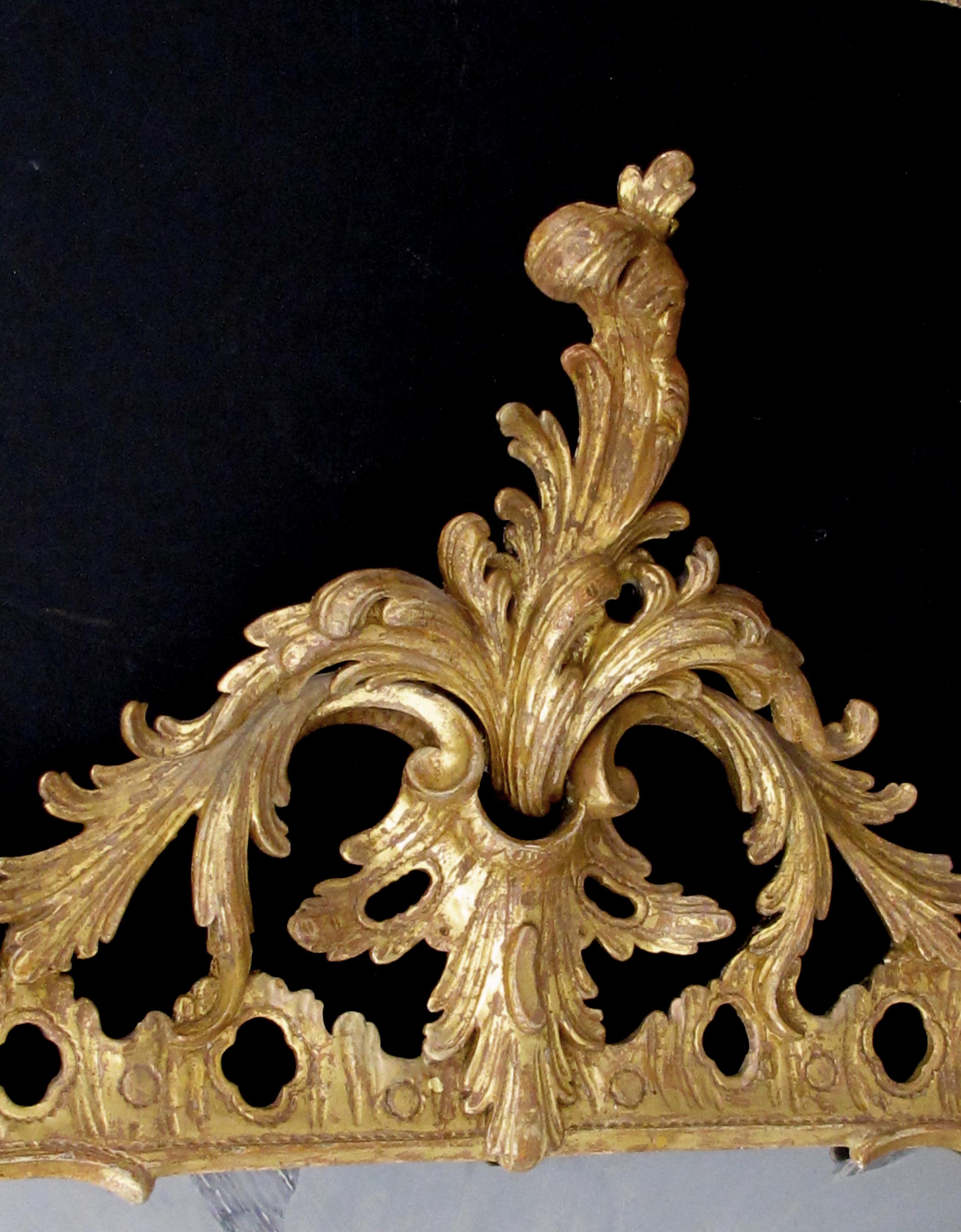 An elegant and superbly carved English George II giltwood mirror with elaborate foliate crest; the finely-carved reticulated frame with exuberant foliate crest; the frame adorned with lively c-scrolls, rocaille and floral motifs; later antique