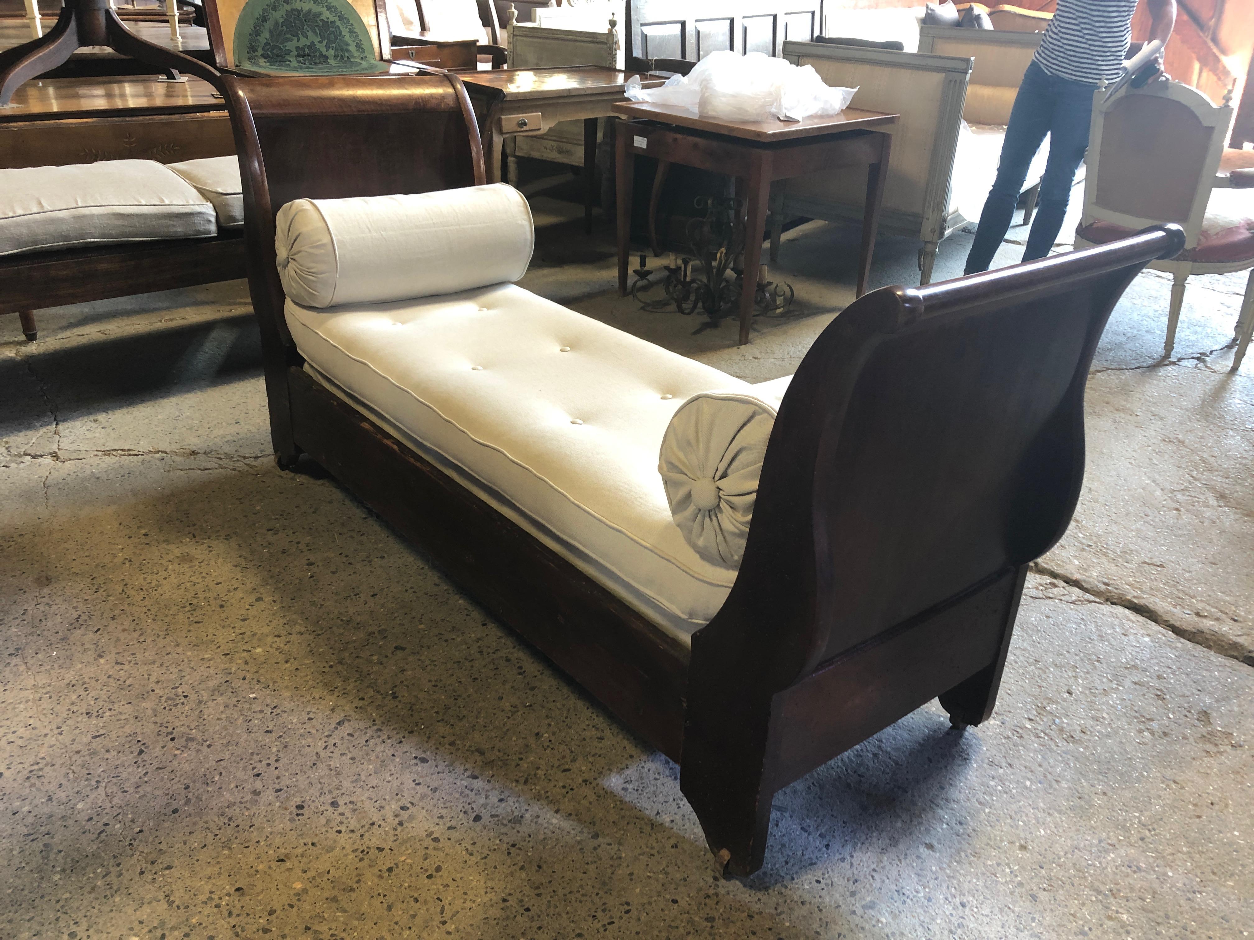 A show stopper elegant French Empire 19th century mahogany daybed, long curvy and sleek, having neoclassical bronze embellishments and crisp new British cotton linen blend upholstery with generous lumbar pillows. The original wooden casters add to