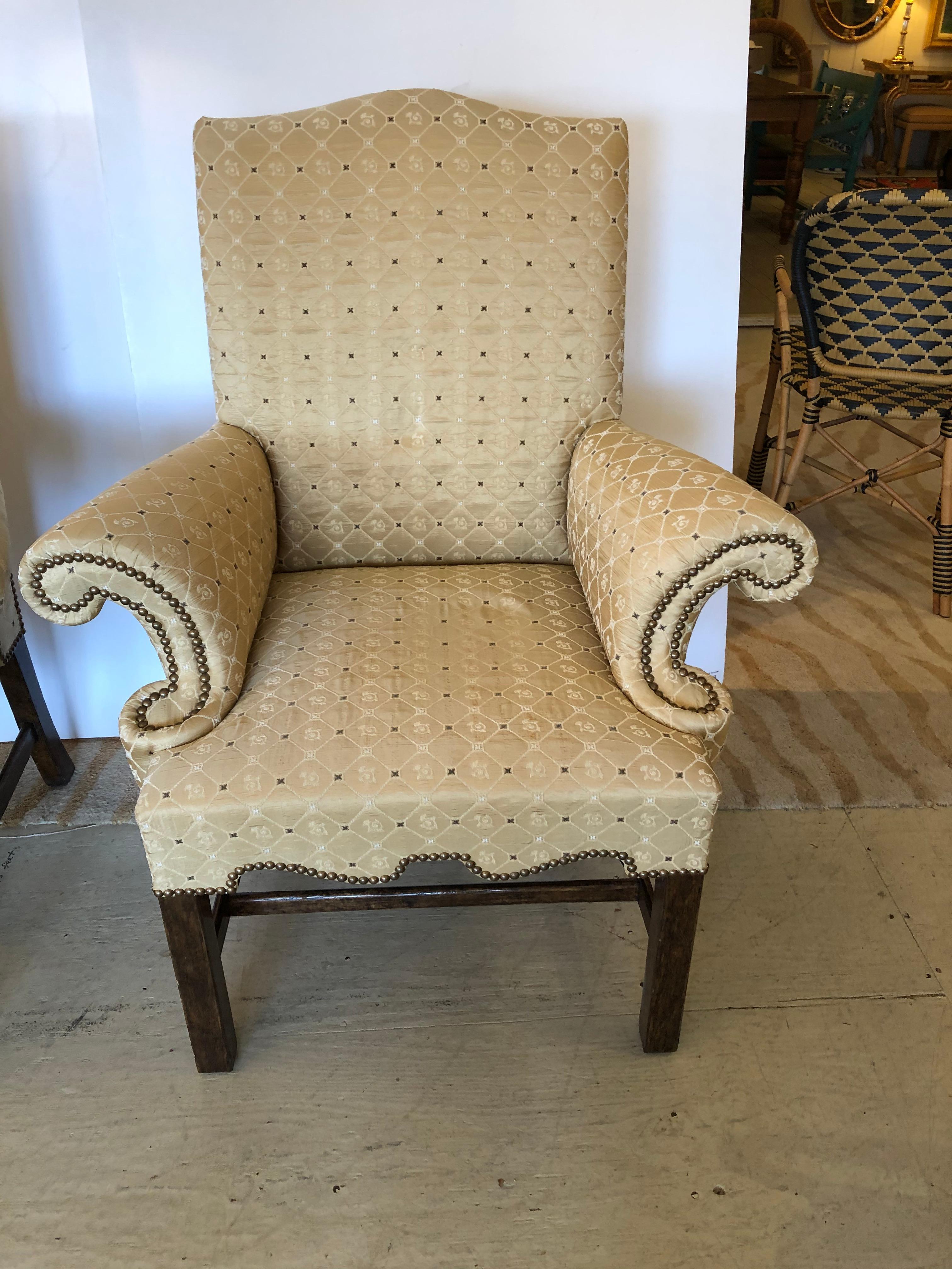 A wonderfully shaped pair of upholstered club or host chairs having dramatic scrolled arms and scalloped decorative apron on Chippendale style straight mahogany legs. Sumptuous gold satiny patterned fabric, unfortunately with one rip on an arm,