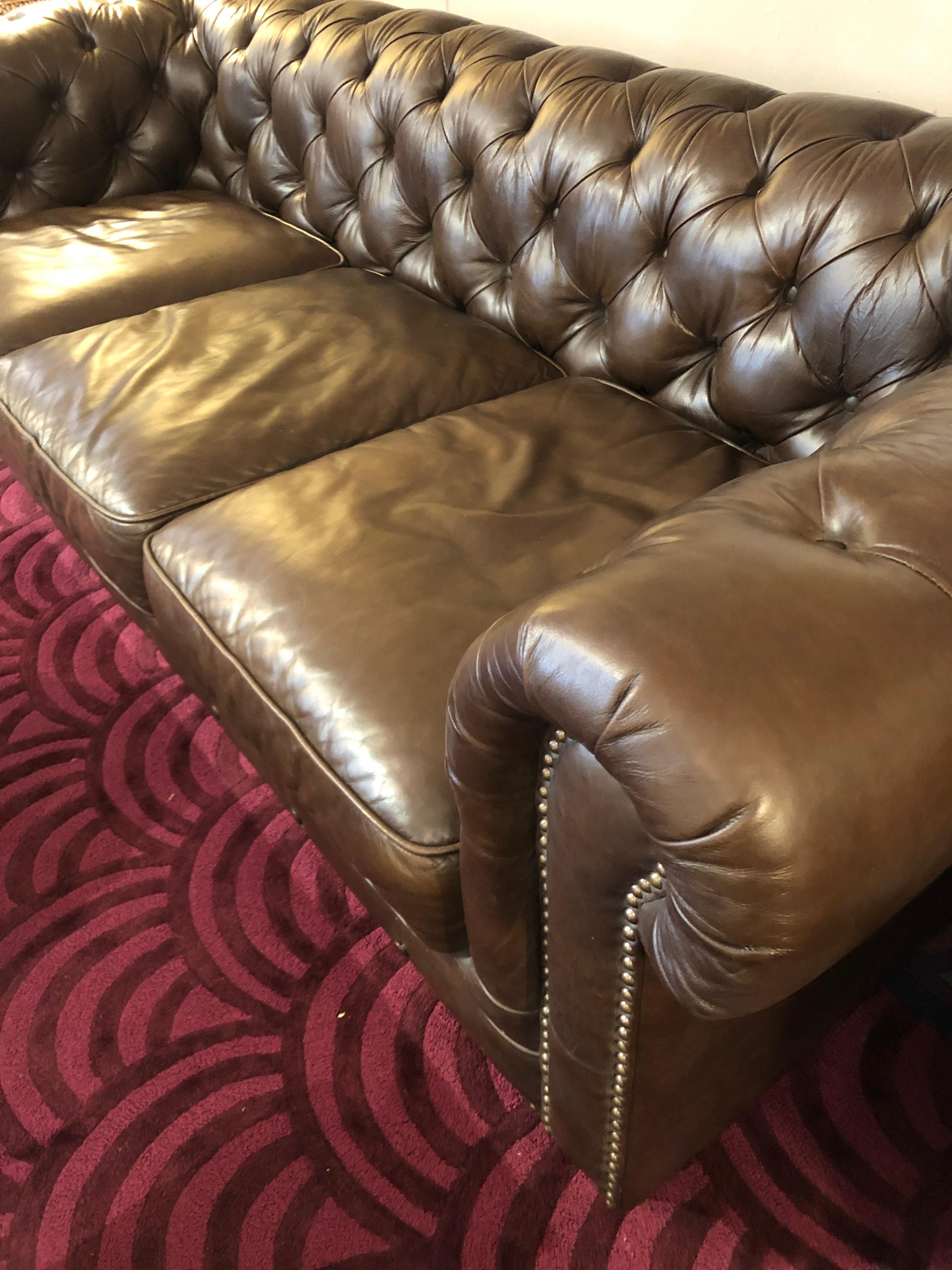 Classic dark chocolately brown leather Chesterfield sofa having tufting on the interior back and arms, 3 very comfortable seat cushions, buttons around the base and brass nailhead detailing. No label. Measures: 8 foot long.