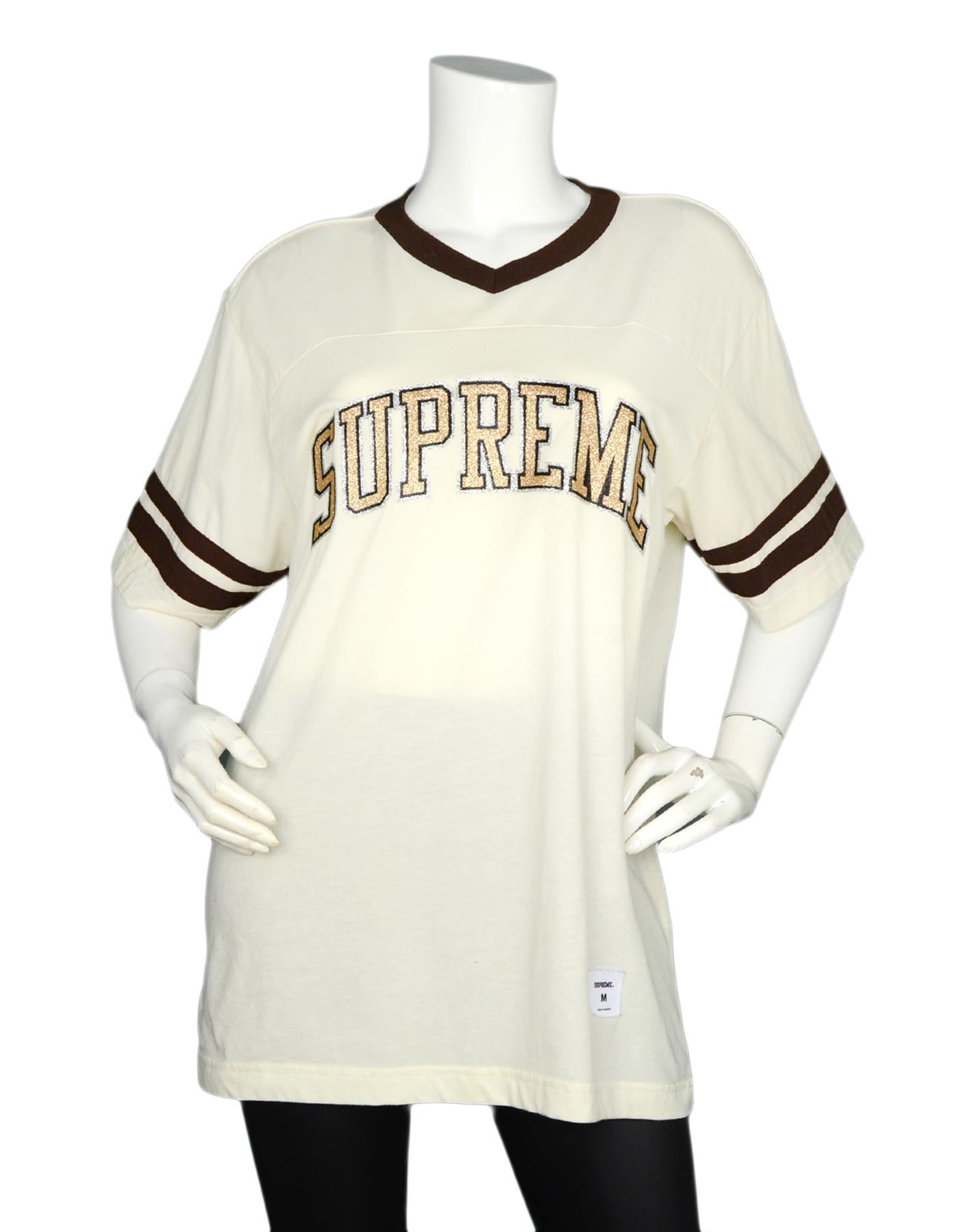 Supreme Men's Beige Glitter Logo Arc Football T-Shirt Sz M

Made In: China 
Color: Beige/brown, gold/silver/black
Materials: 60% cotton, 40% polyester
Opening/Closure: Pull over
Overall Condition: Excellent pre-owned condition
Measurements: