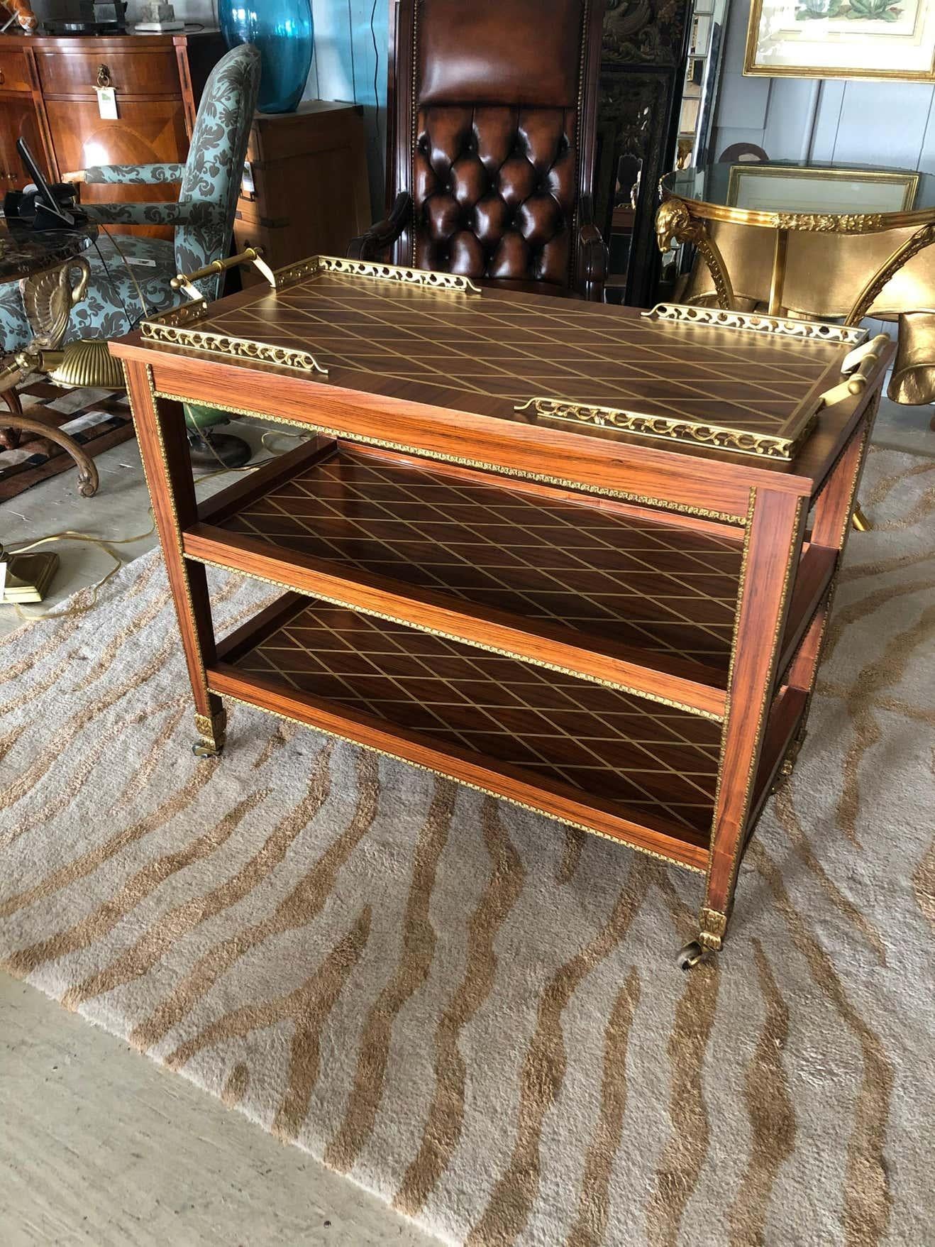 An unusually elegant mixed wood inlay bar cart having gorgeous criss cross design on each of the 3 tiers as well as rich matte brass galleries and handles. Even the caps on the tapered legs are sumptuously decorative. Rolls smoothly on casters, but